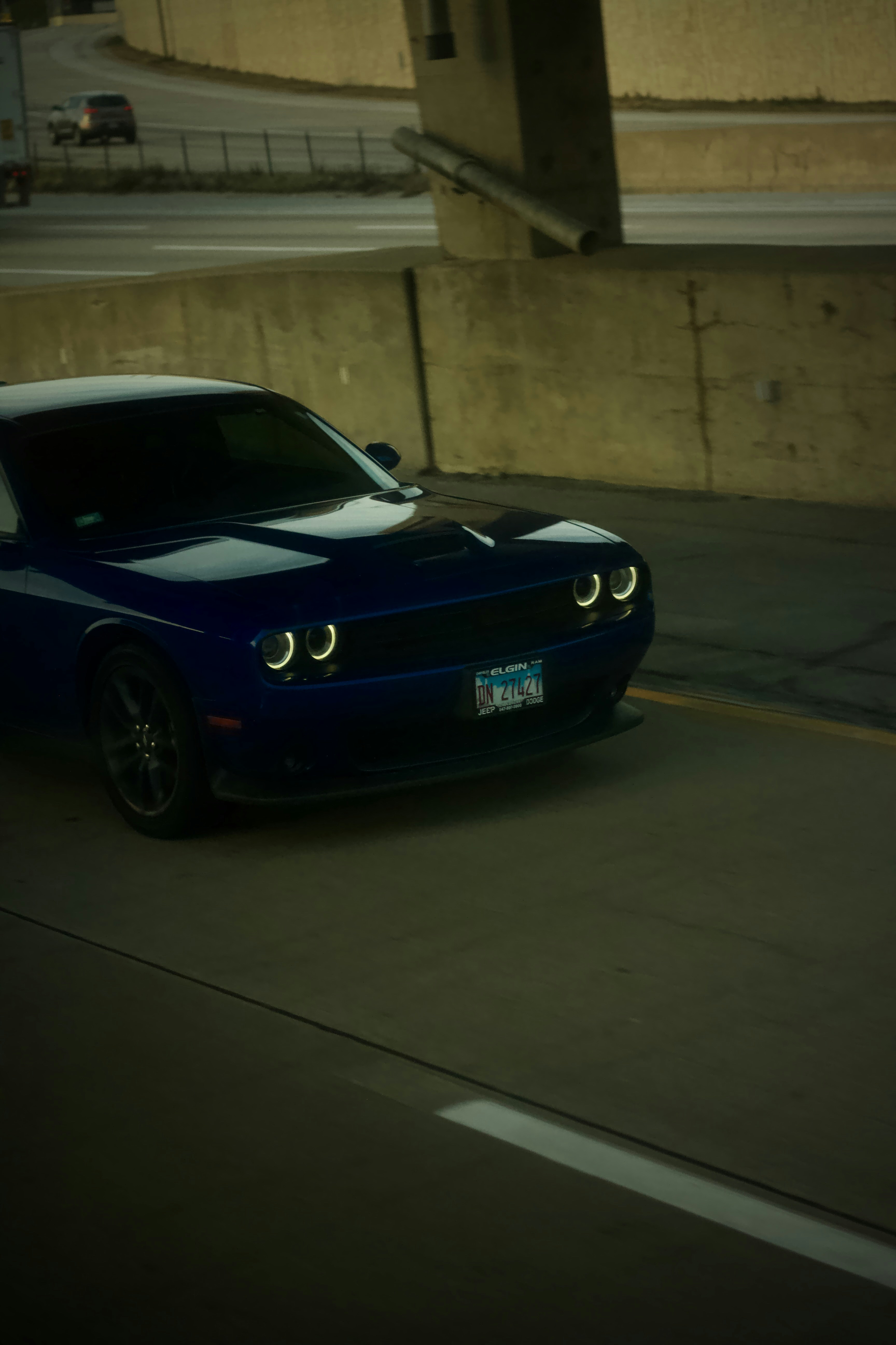 A blue car driving down a street next to a bridge