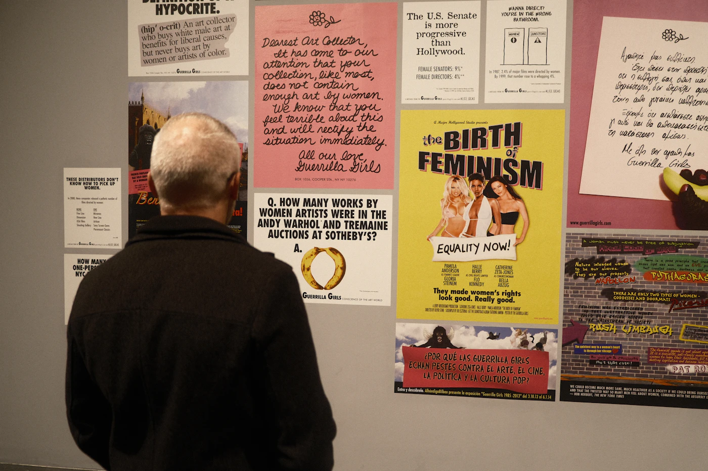 A wall of exhibition posters and printed notices layered edge to edge in a gallery corridor