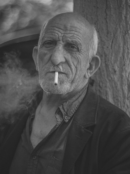 A man smoking a cigarette next to a tree