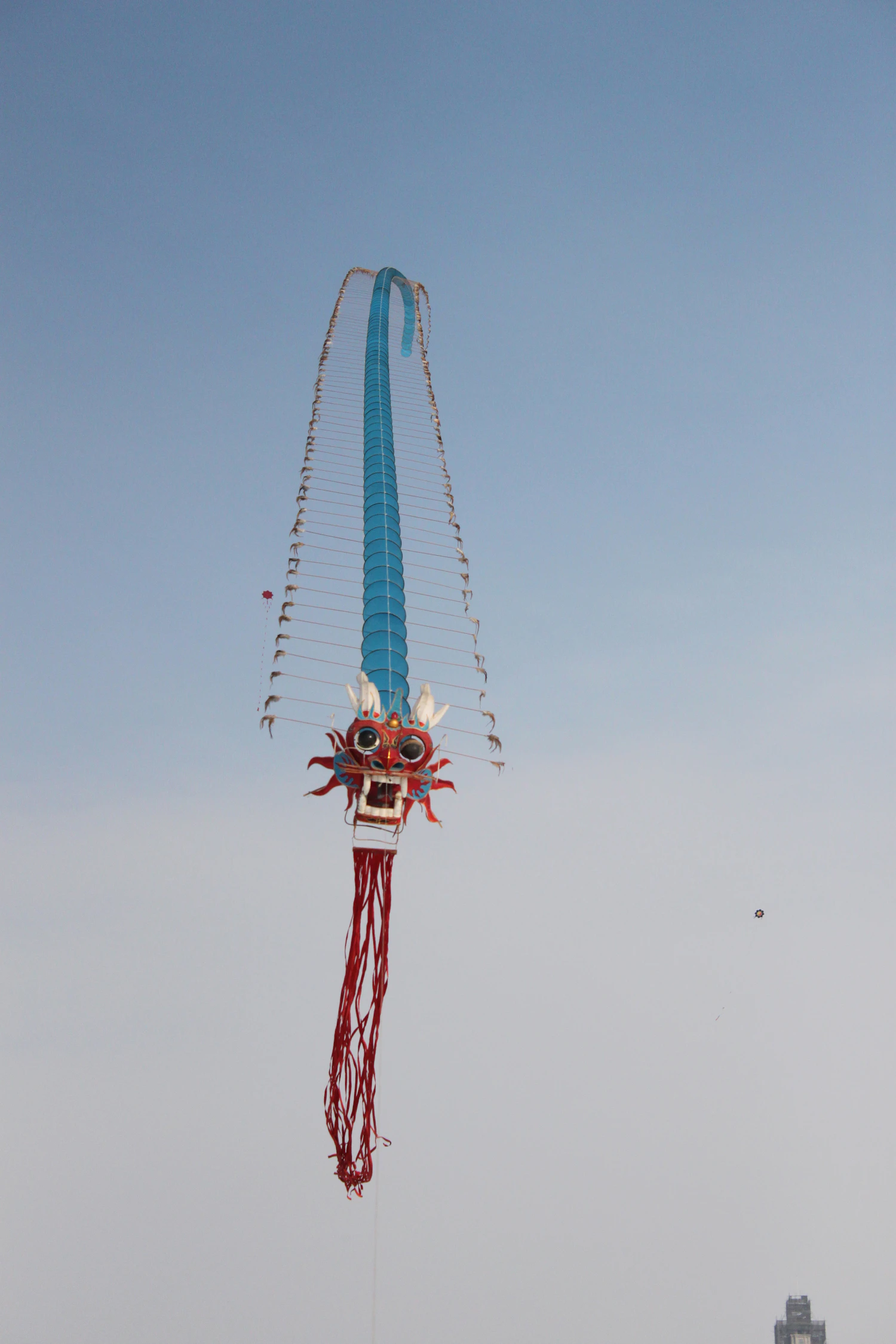 A dragon centipede kite hanging straight down the sky from its painted head