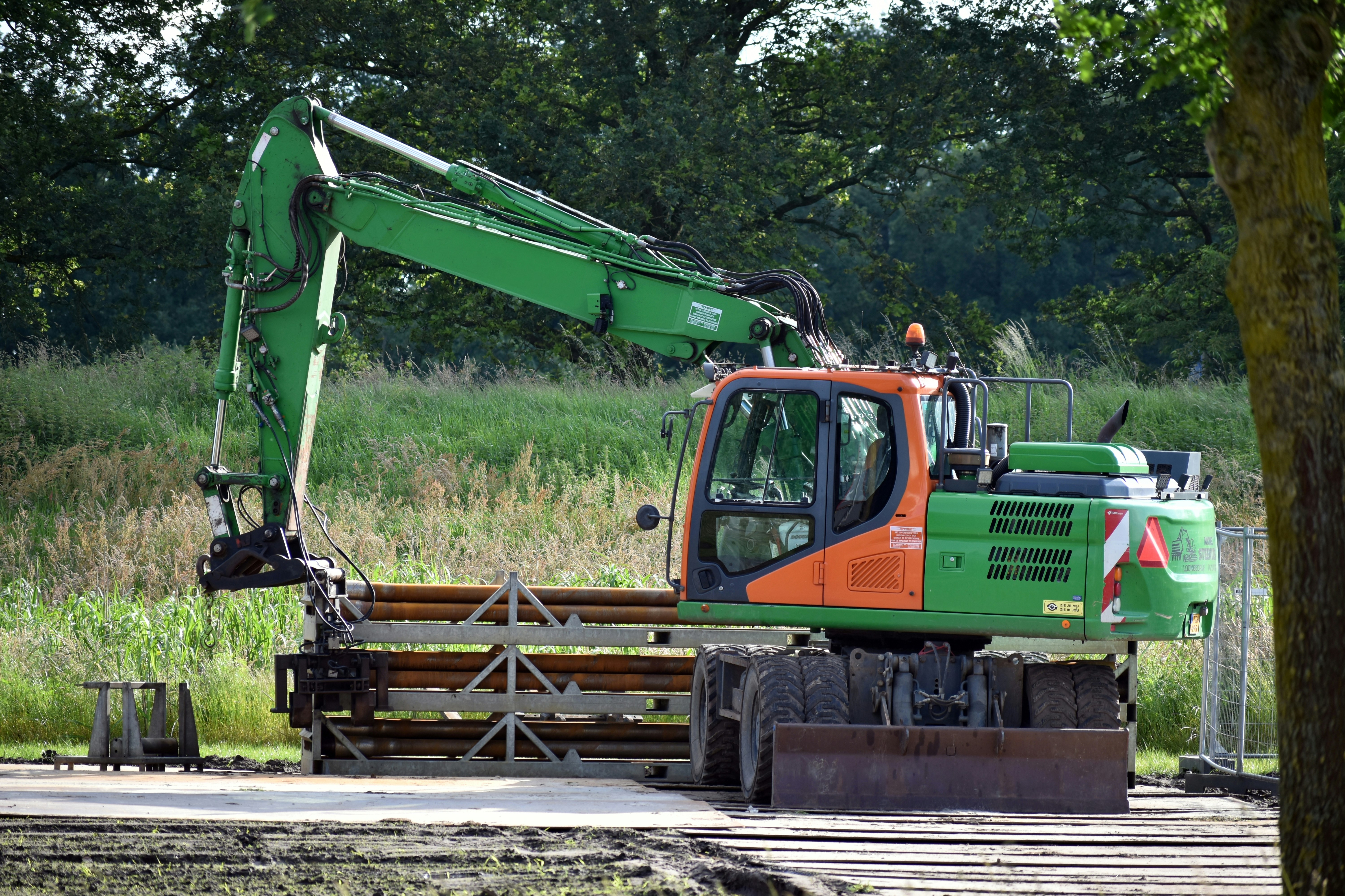 A green and orange truck parked next to a forest