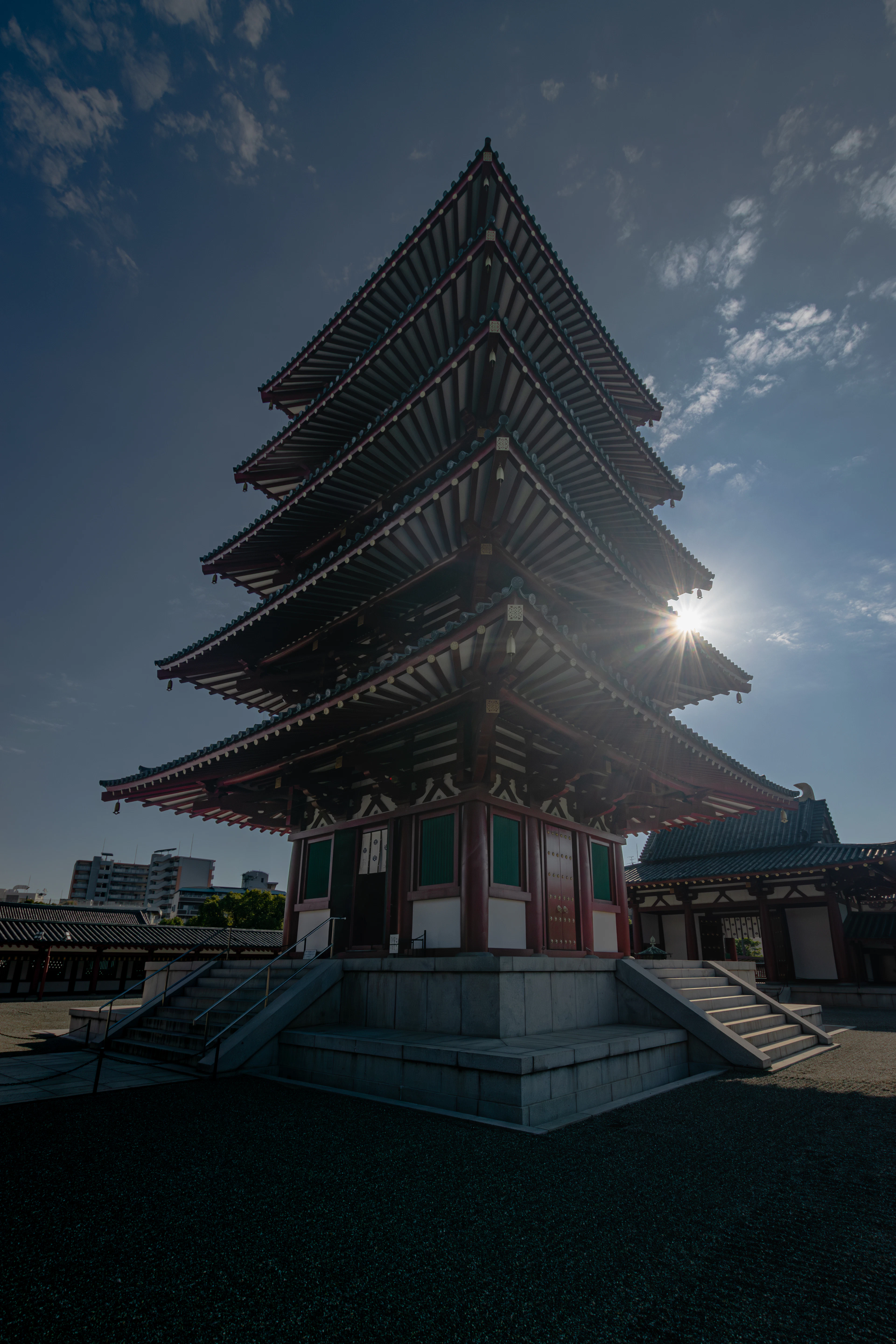 A five-story pagoda at Shitenno-ji Temple is silhouetted against the sun and blue sky.
