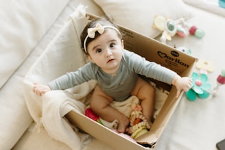 A little girl sitting inside of a box on a bed