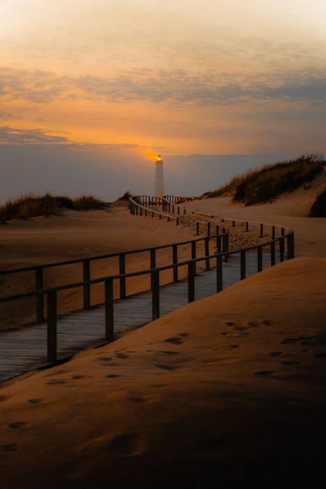 A boardwalk path leading toward a lighthouse at the coast