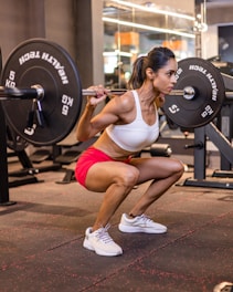 A woman squats in a gym with a barbell