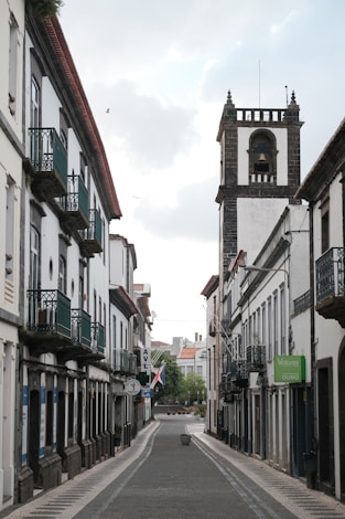 A narrow street with a clock tower in the background