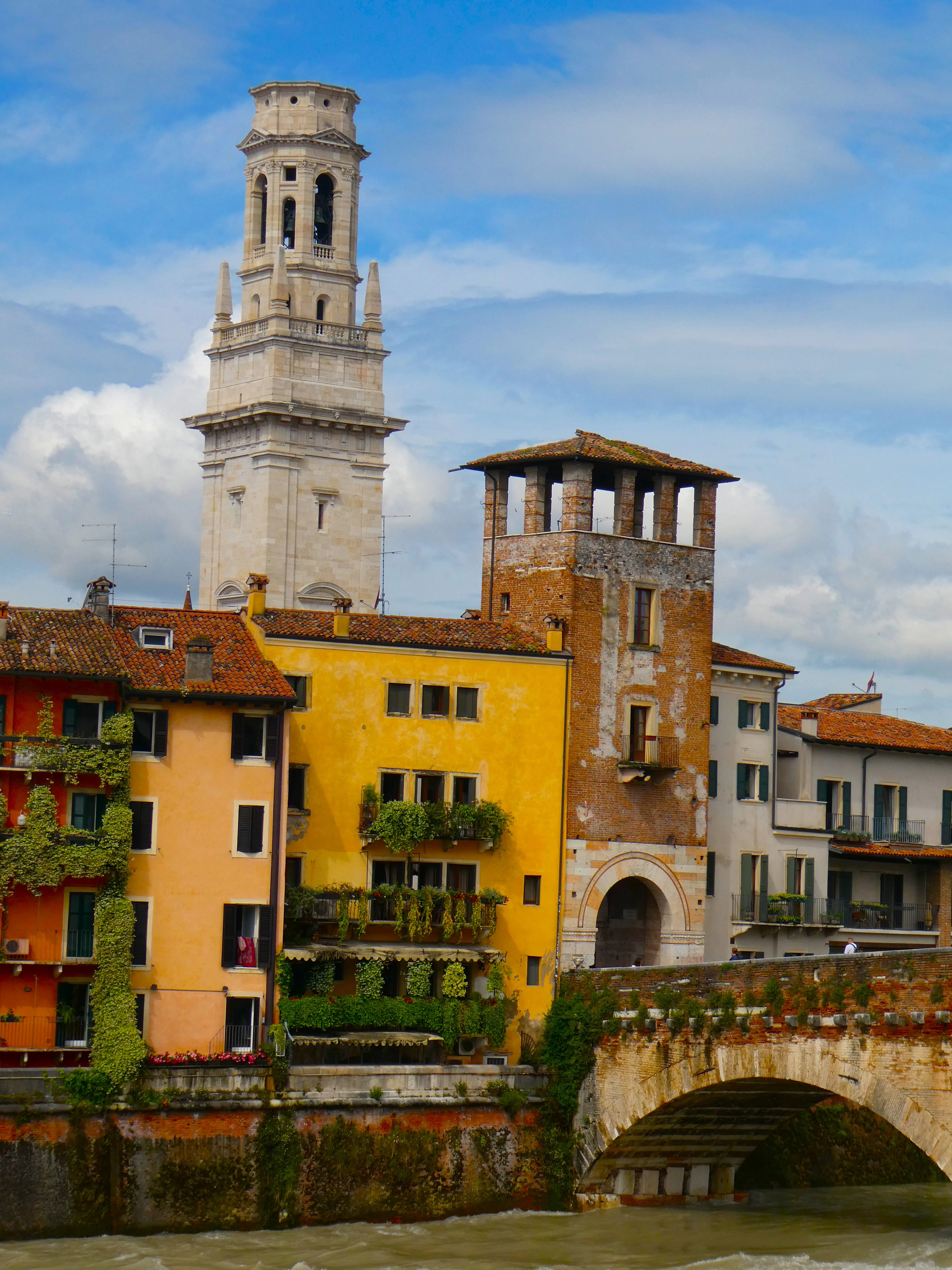 Colorful ochre and yellow riverside houses along the Adige, with a white bell tower rising behind them.
