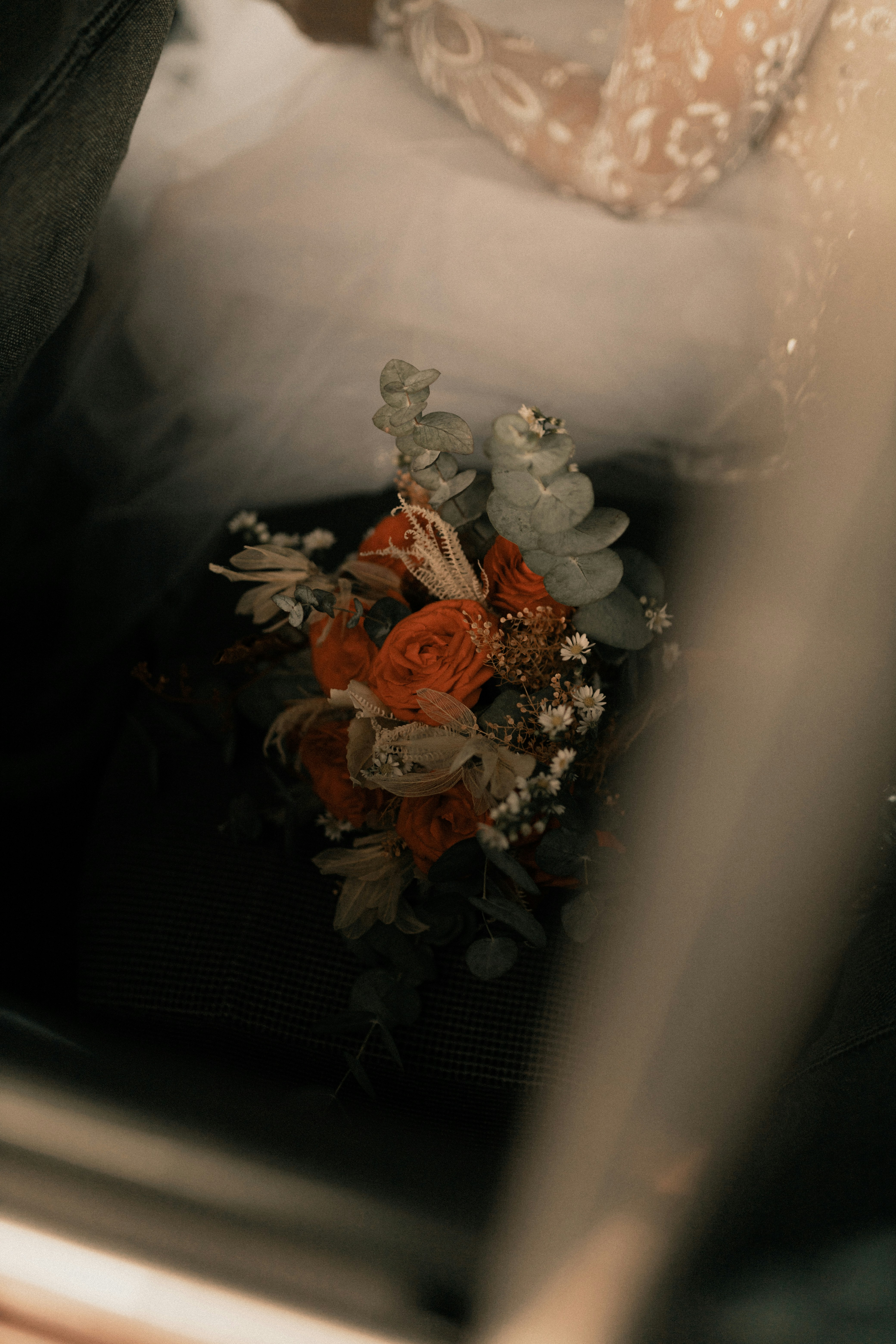 Florist carefully arranging a bouquet of garden roses and eucalyptus on a wooden workbench in a dark studio