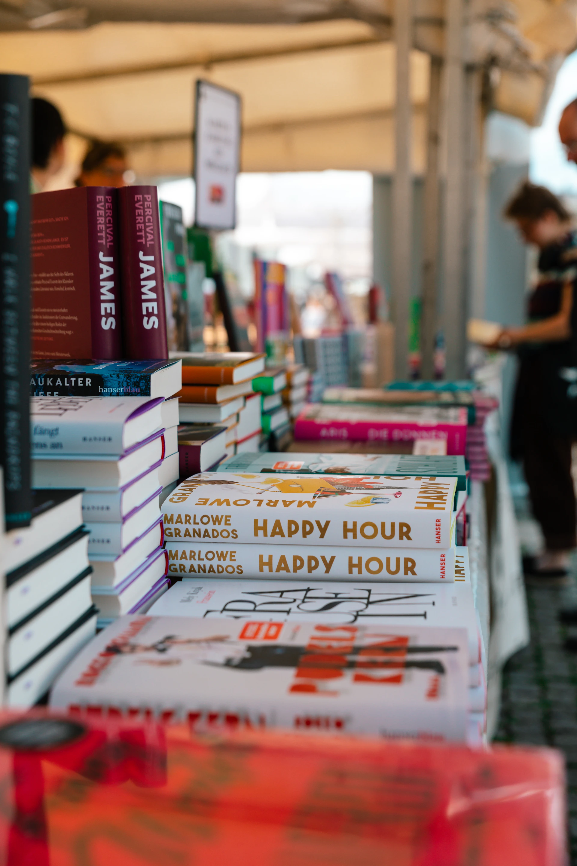 A number of books on a table with people in the background