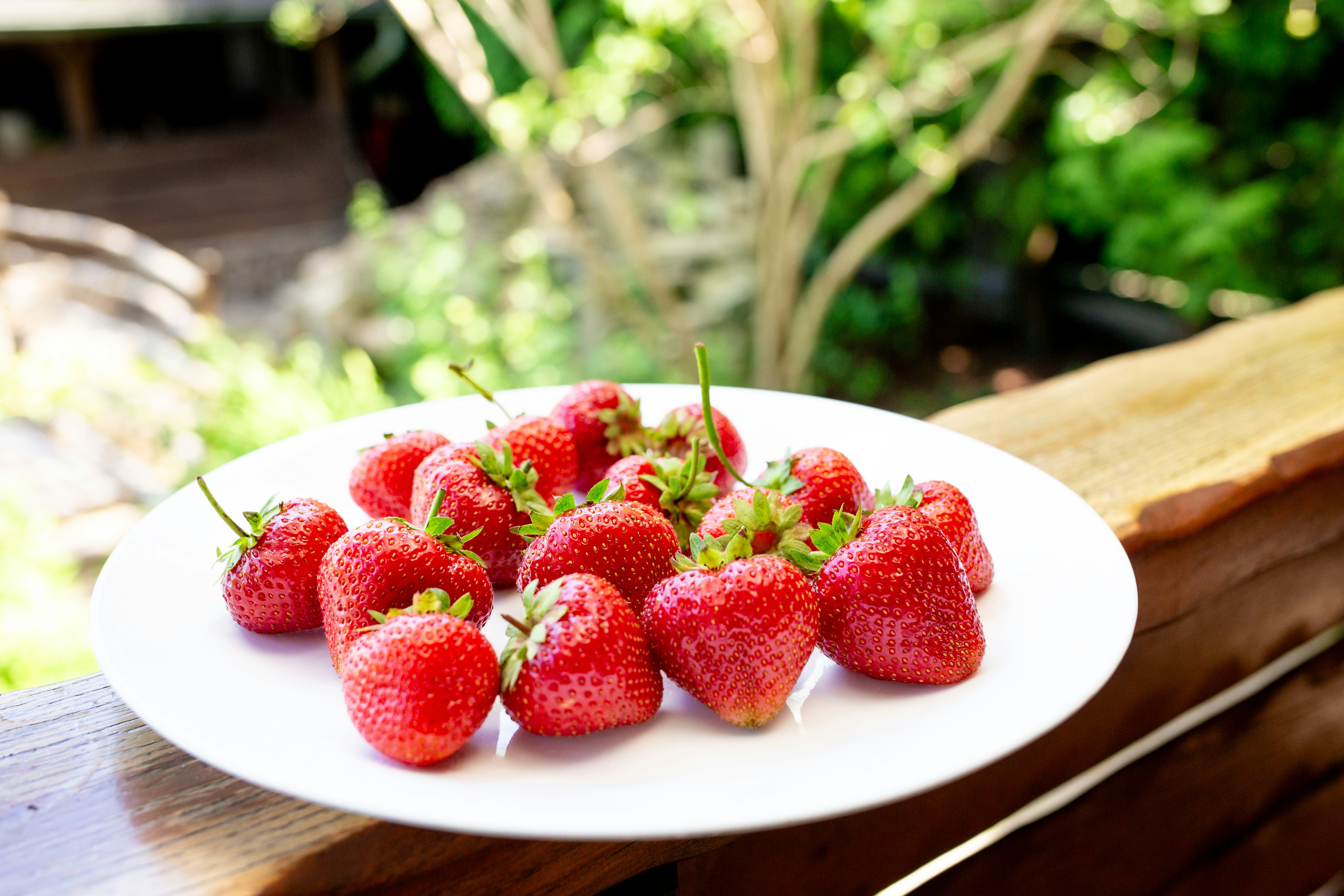 A plate of strawberries sitting on a wooden bench