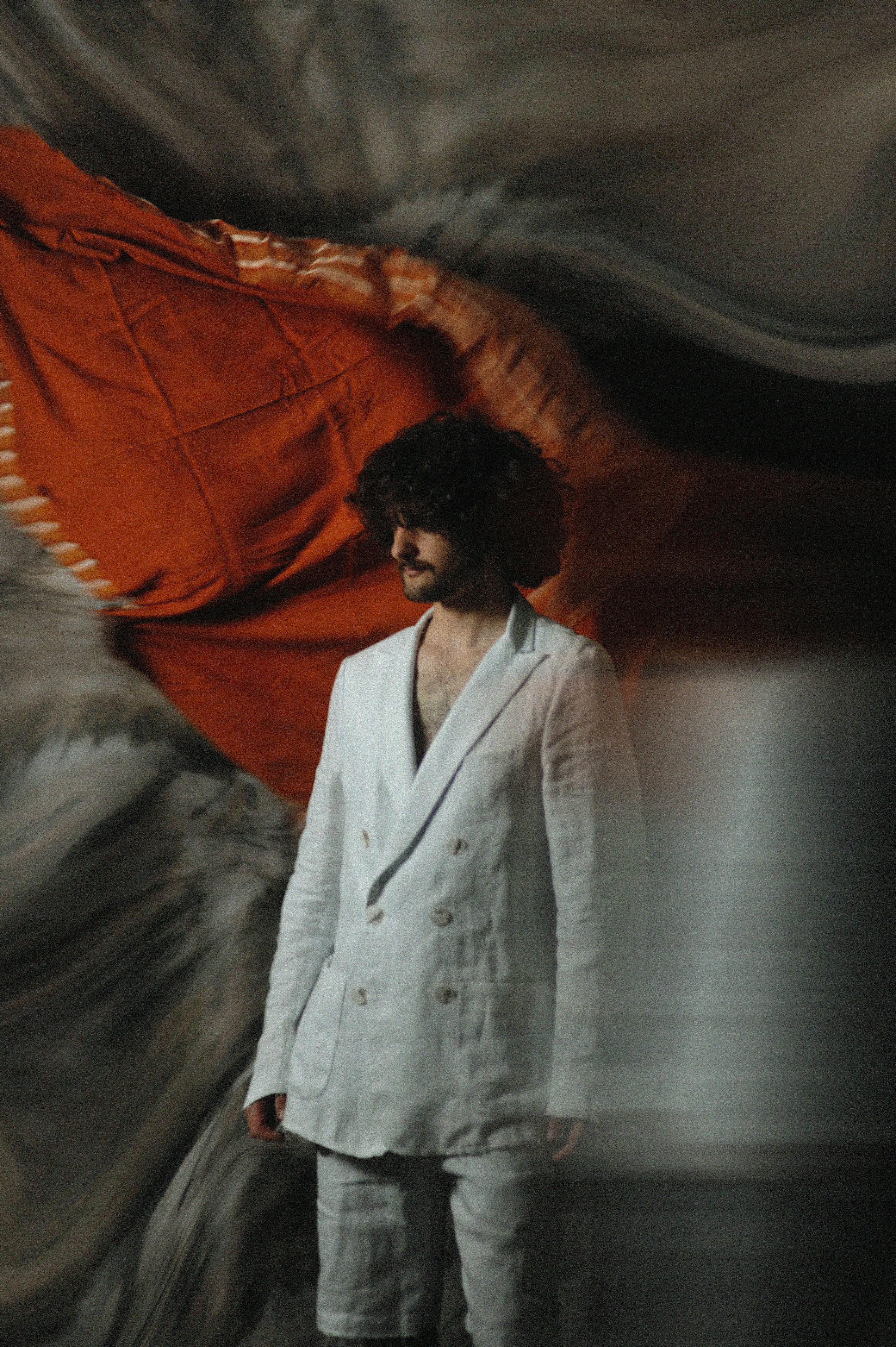 A man in a white suit standing in front of a red flag