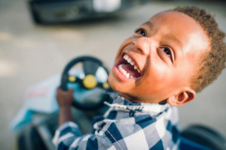 A young boy smiles while driving a toy car