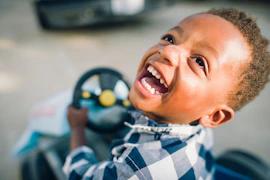 A young boy smiles while driving a toy car