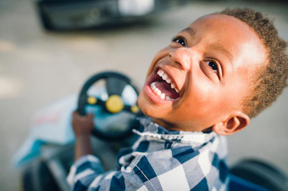 A young boy smiles while driving a toy car