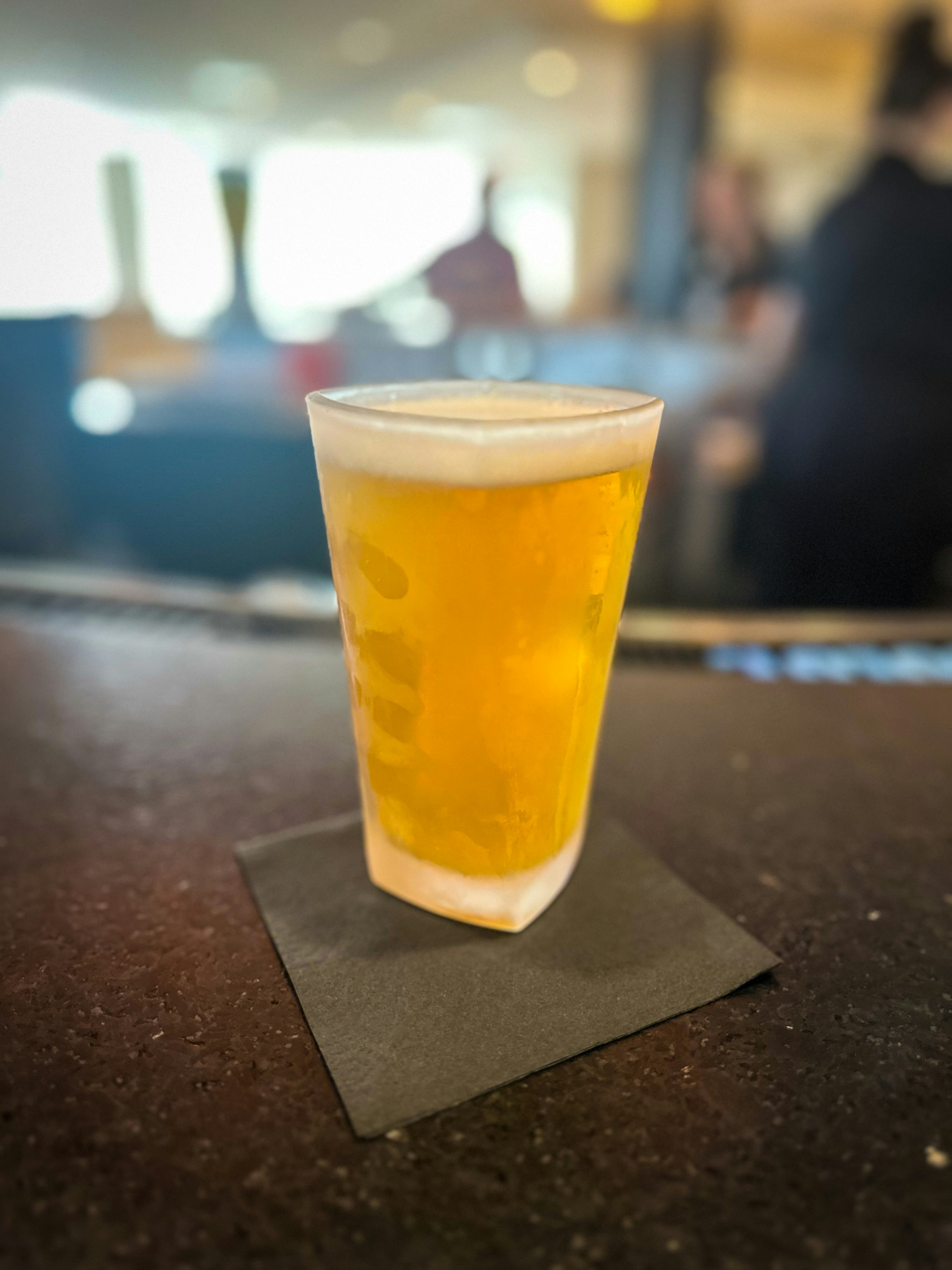 Craft beer pint glass with golden lager and thick foam head, dim bar lighting