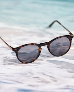 A pair of sunglasses sitting on top of a sandy beach