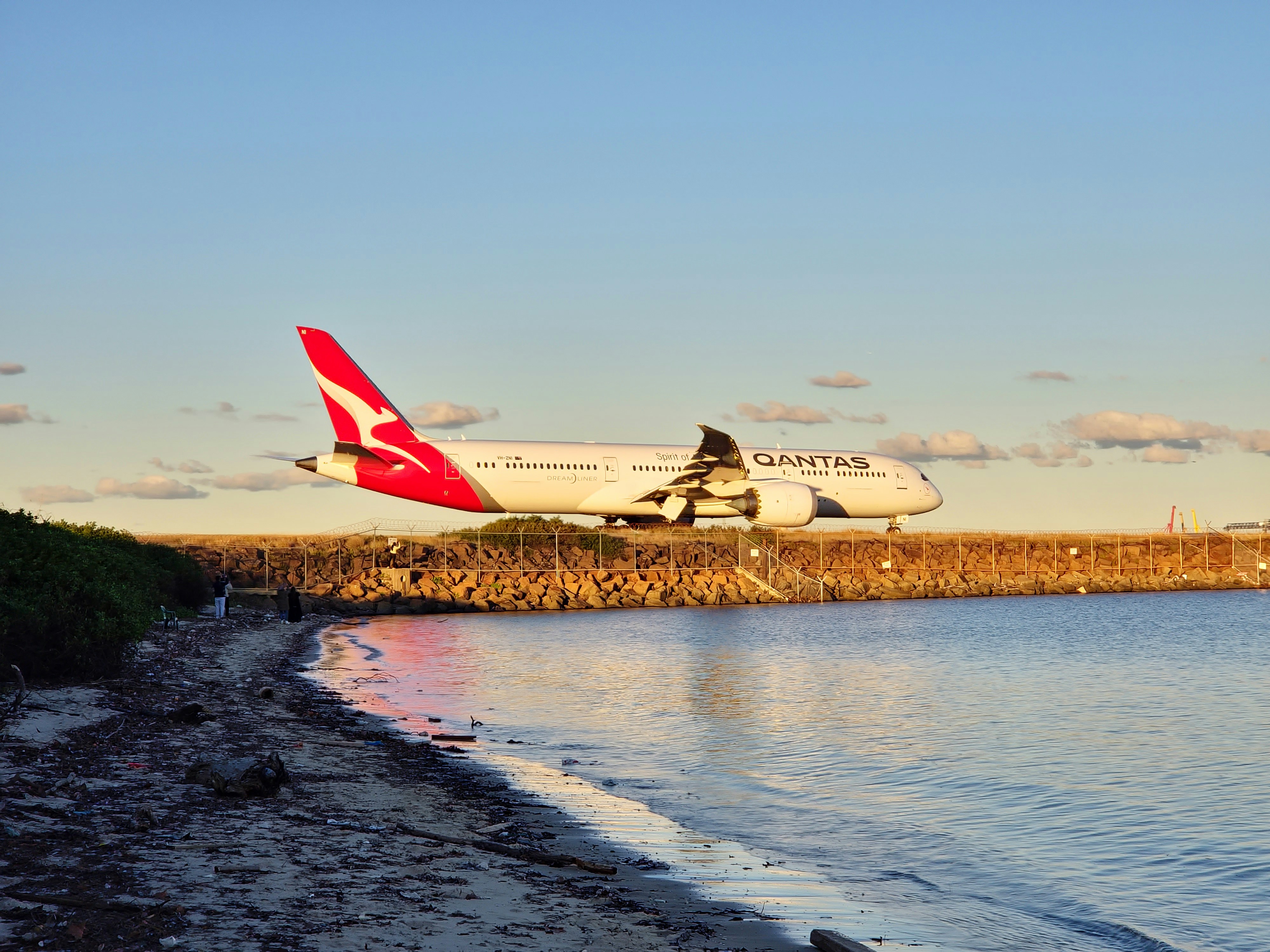 A large jetliner flying over a body of water, Qantas airplane over beach