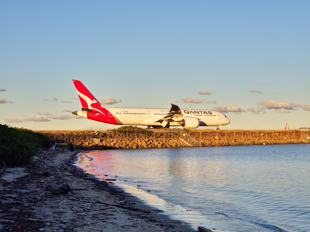A large jetliner flying over a body of water, Qantas airplane over beach
