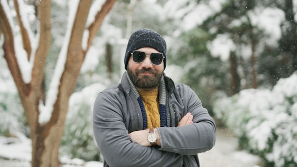 A man wearing a hat and sunglasses standing in the snow