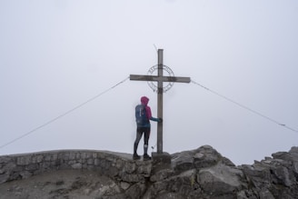 A person standing on top of a mountain next to a cross