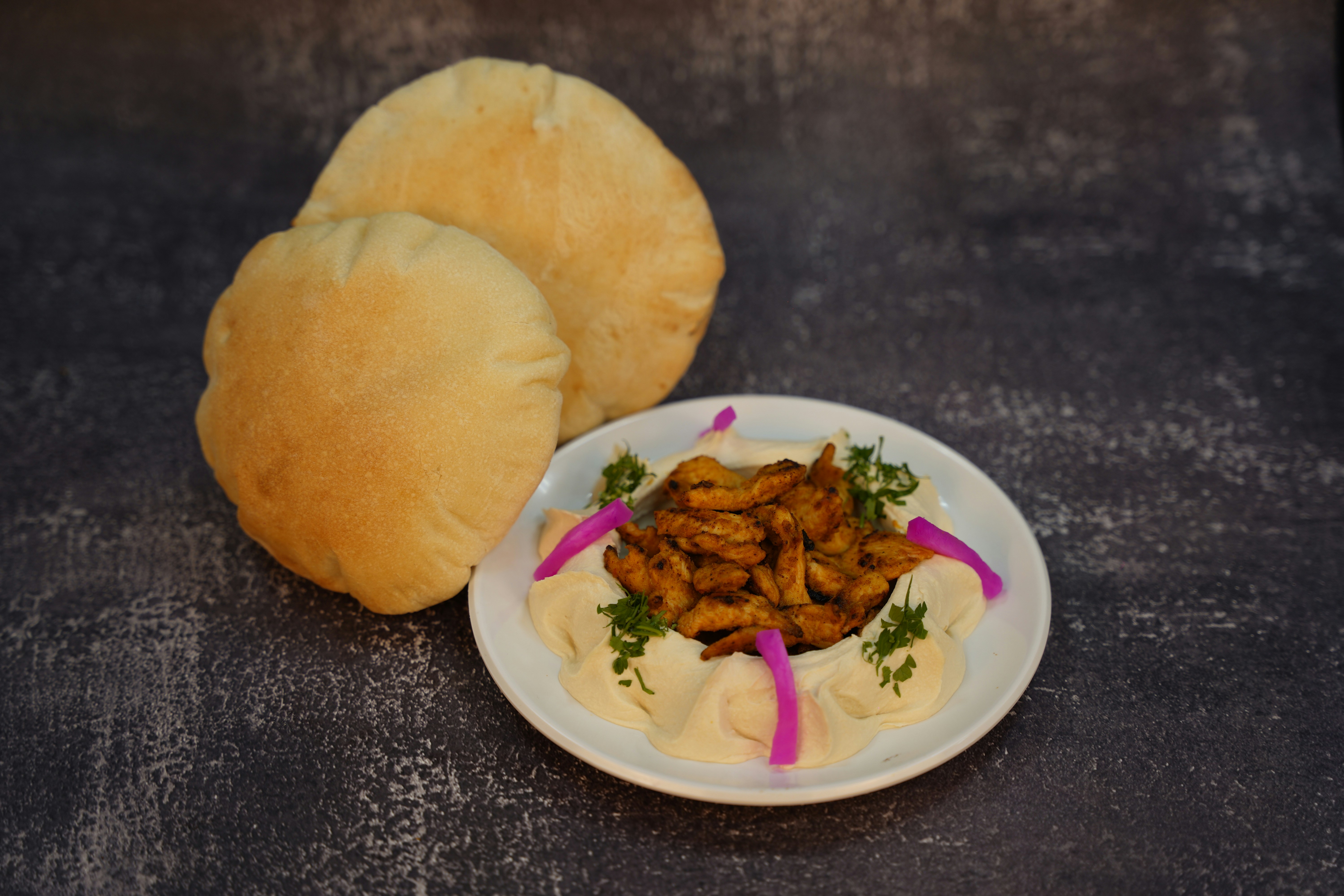 Fresh hummus bowl with olive oil drizzle and pita chips, white background