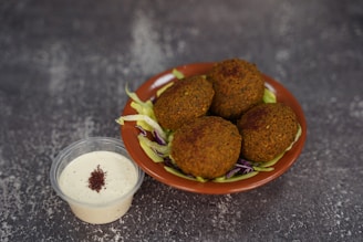 A plate of falafel next to a container of dressing