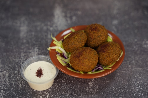A plate of falafel next to a container of dressing