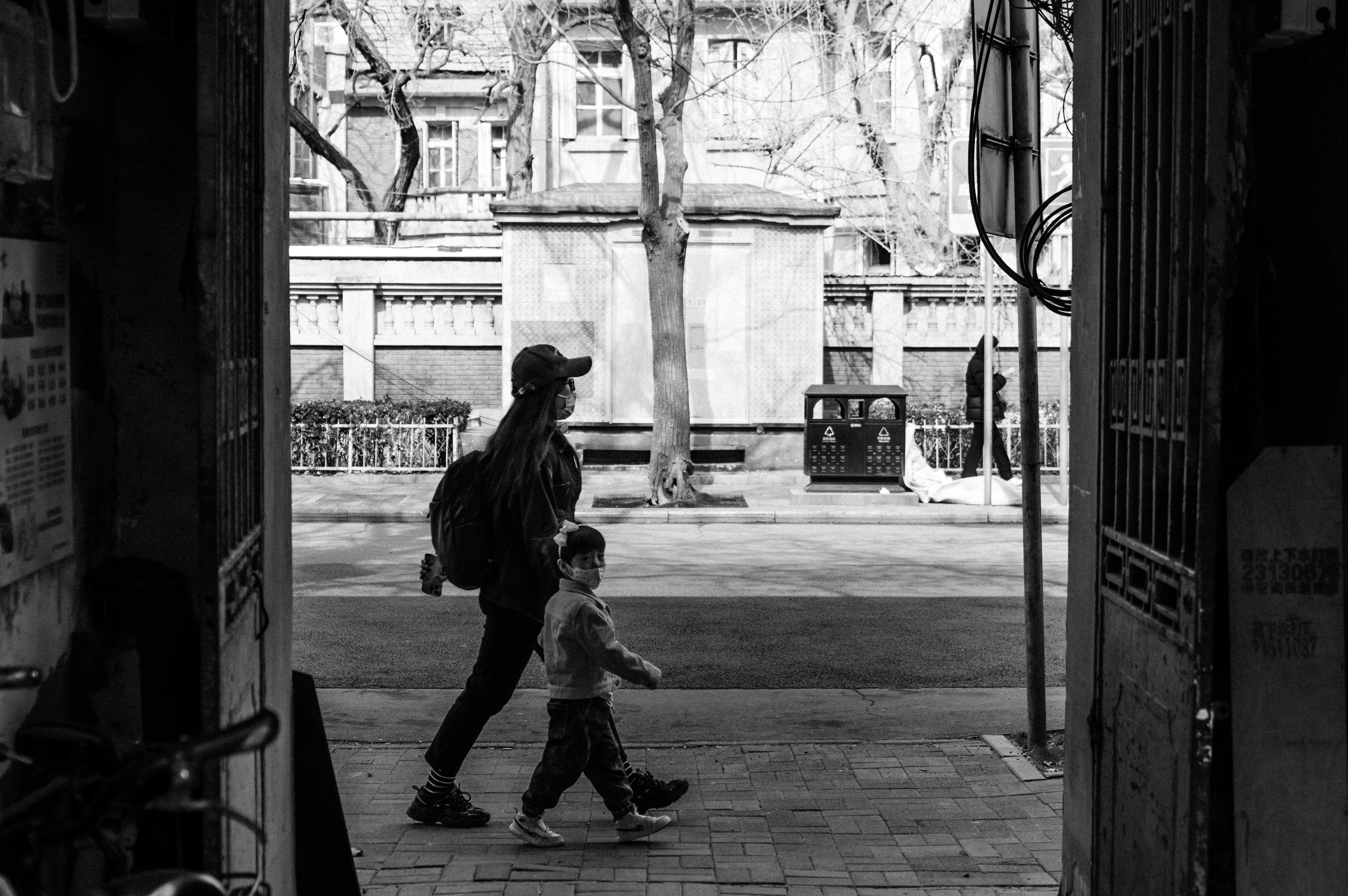 A black and white photo of an adult and a child walking past a doorway on a city sidewalk