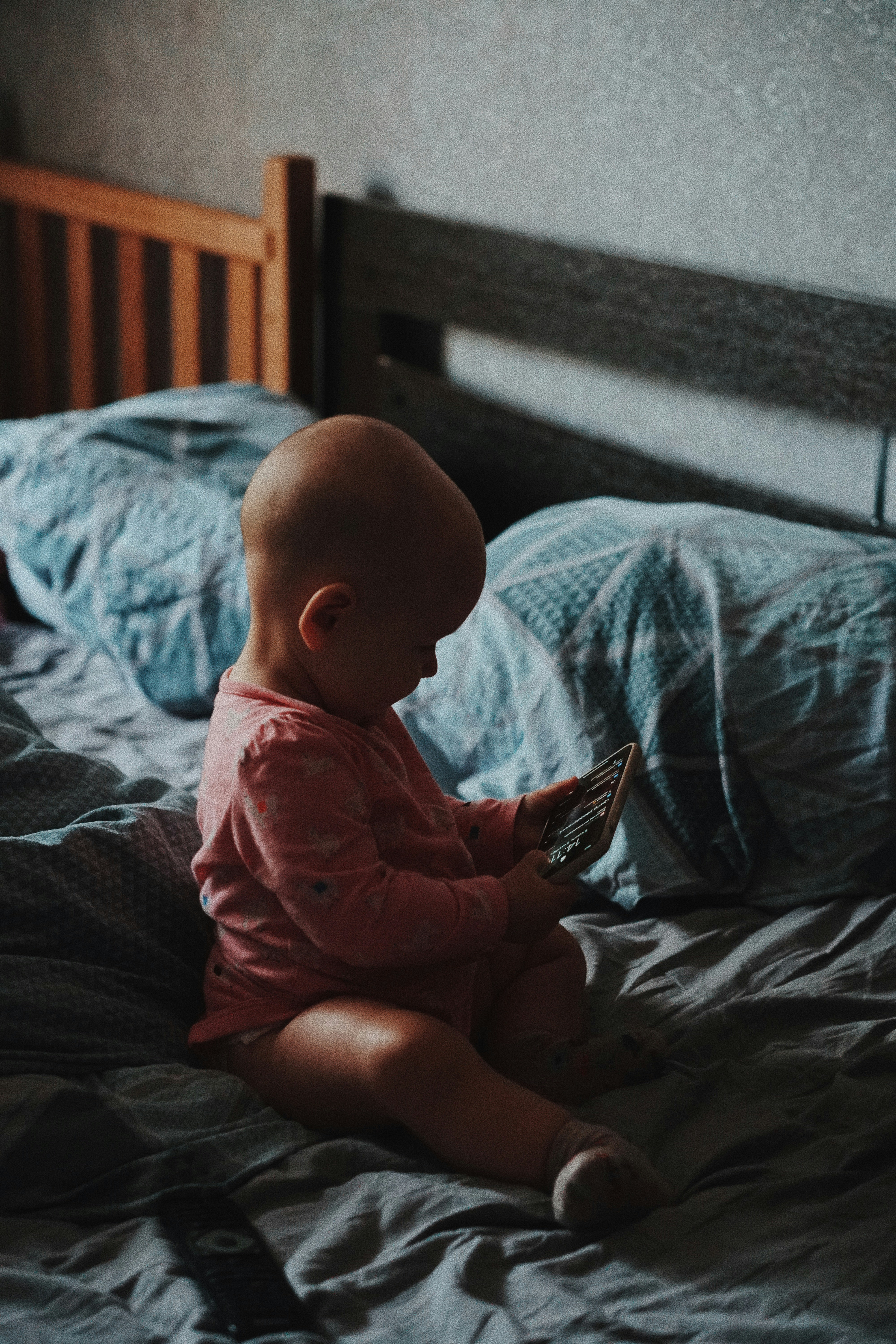 A baby sitting on a bed looking at a book