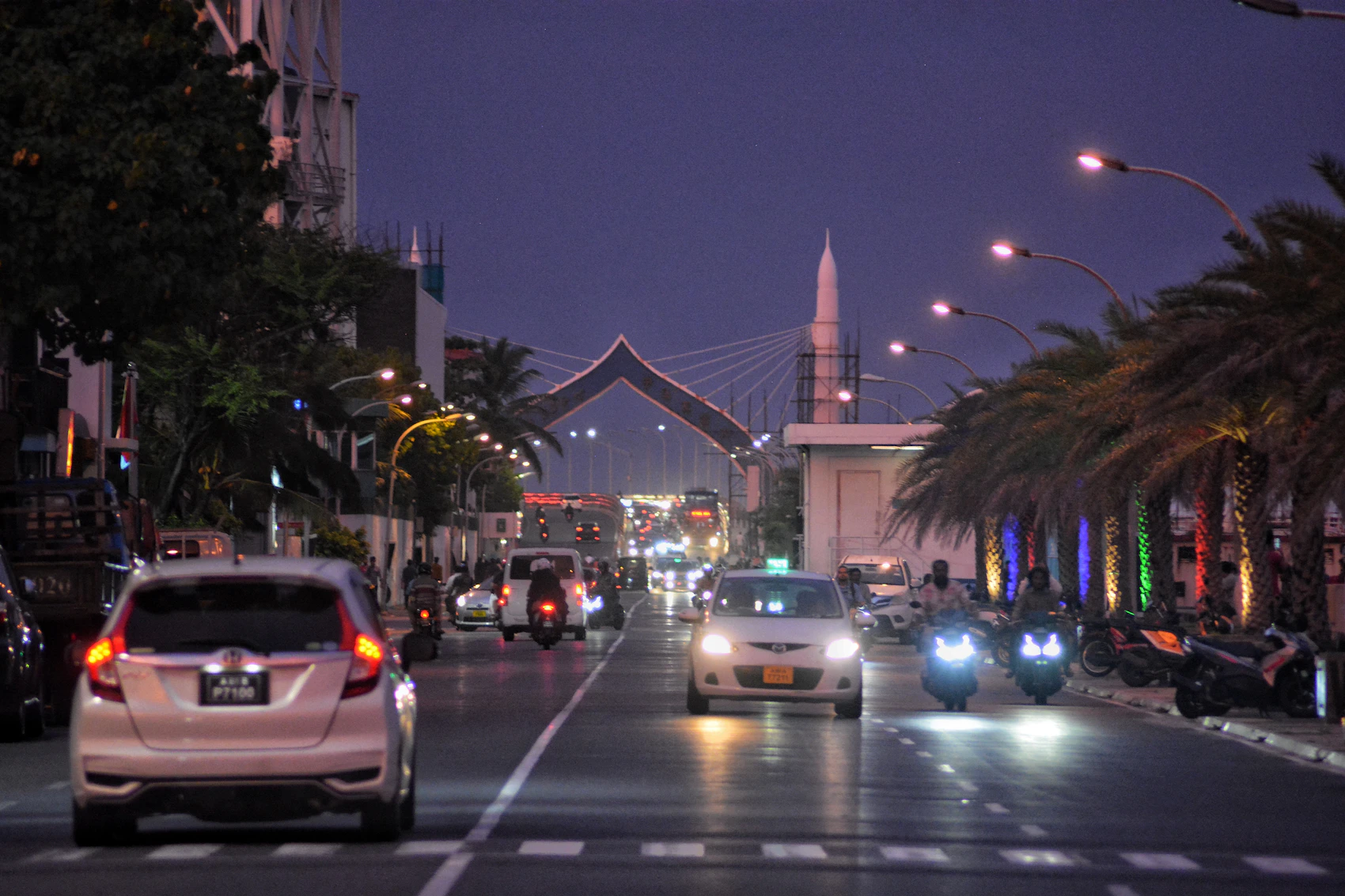 A busy Malé avenue at night with cars, motorbikes, palm trees and mosque architecture