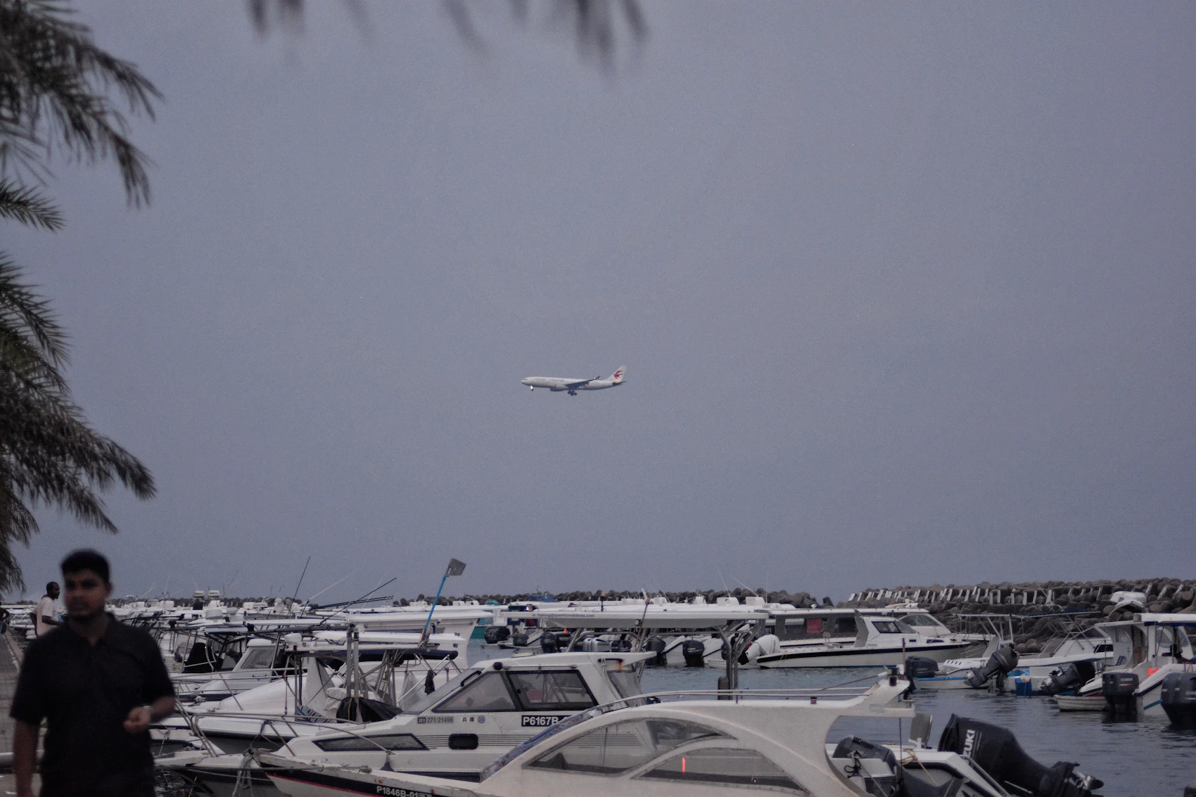 Speedboats gathered at Malé harbour beneath a dark, rain-heavy sky as an aircraft approaches