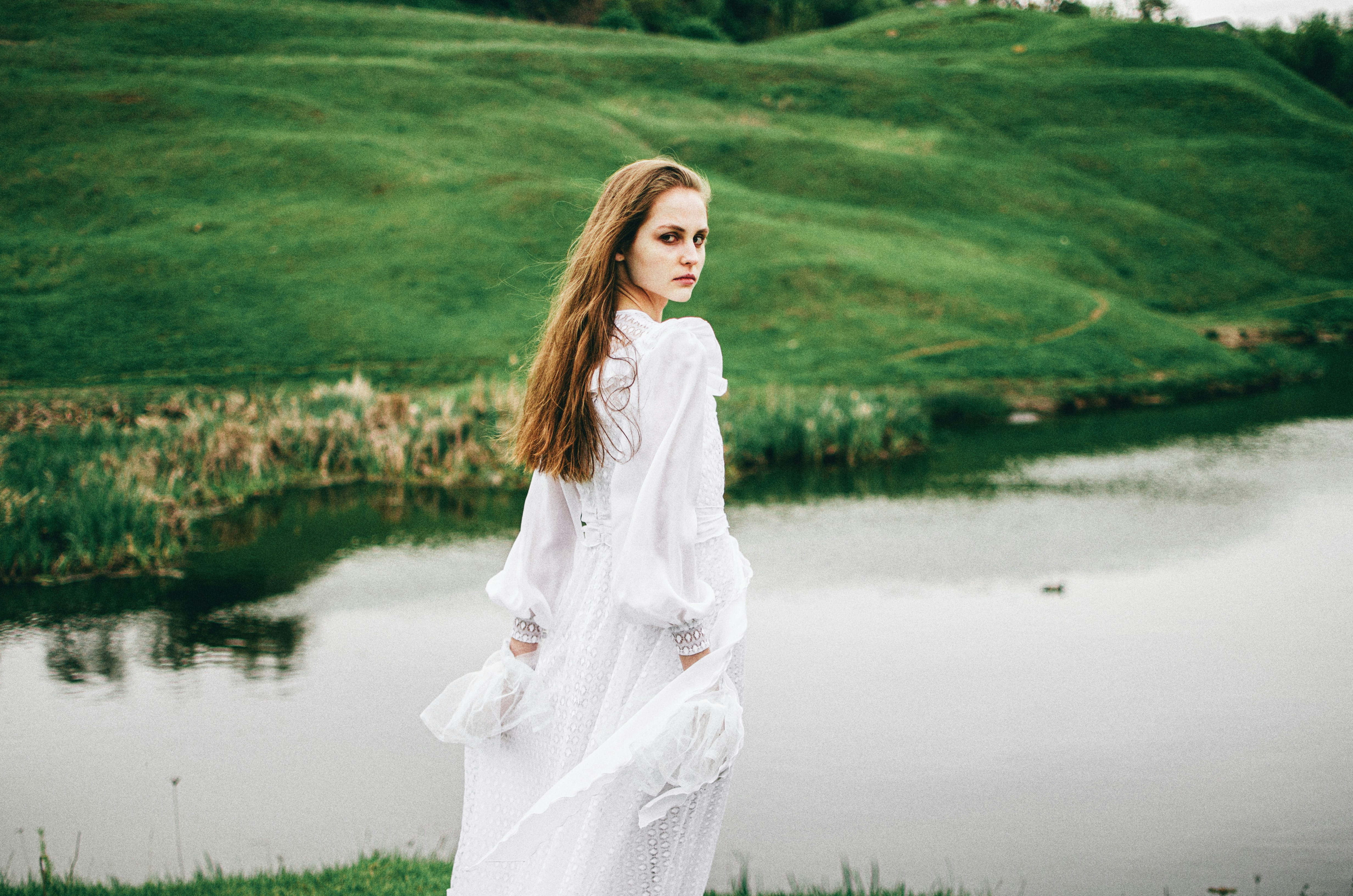 A woman in a white dress standing in front of a lake