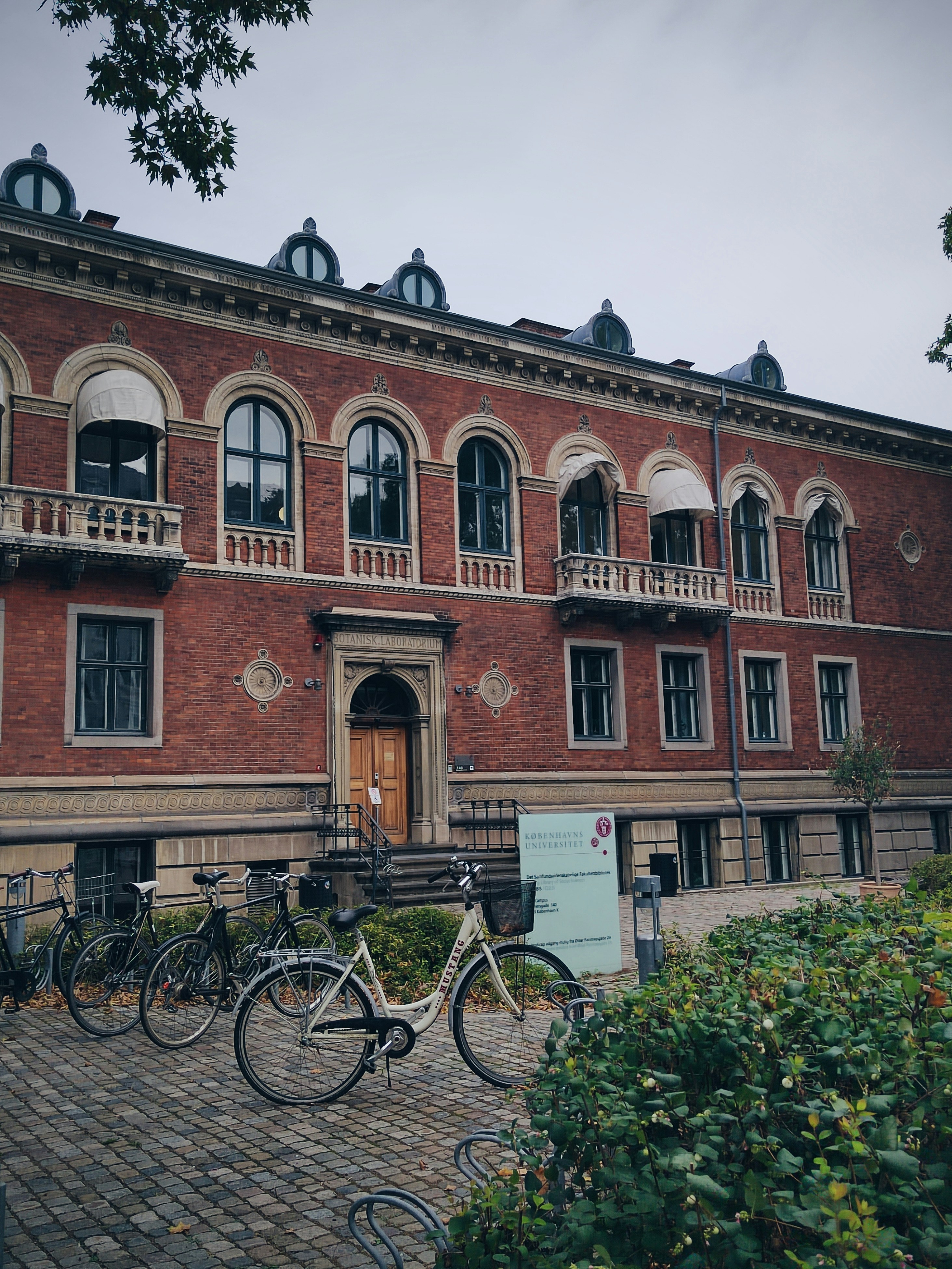 A brick building with many windows and bicycles parked in front of it