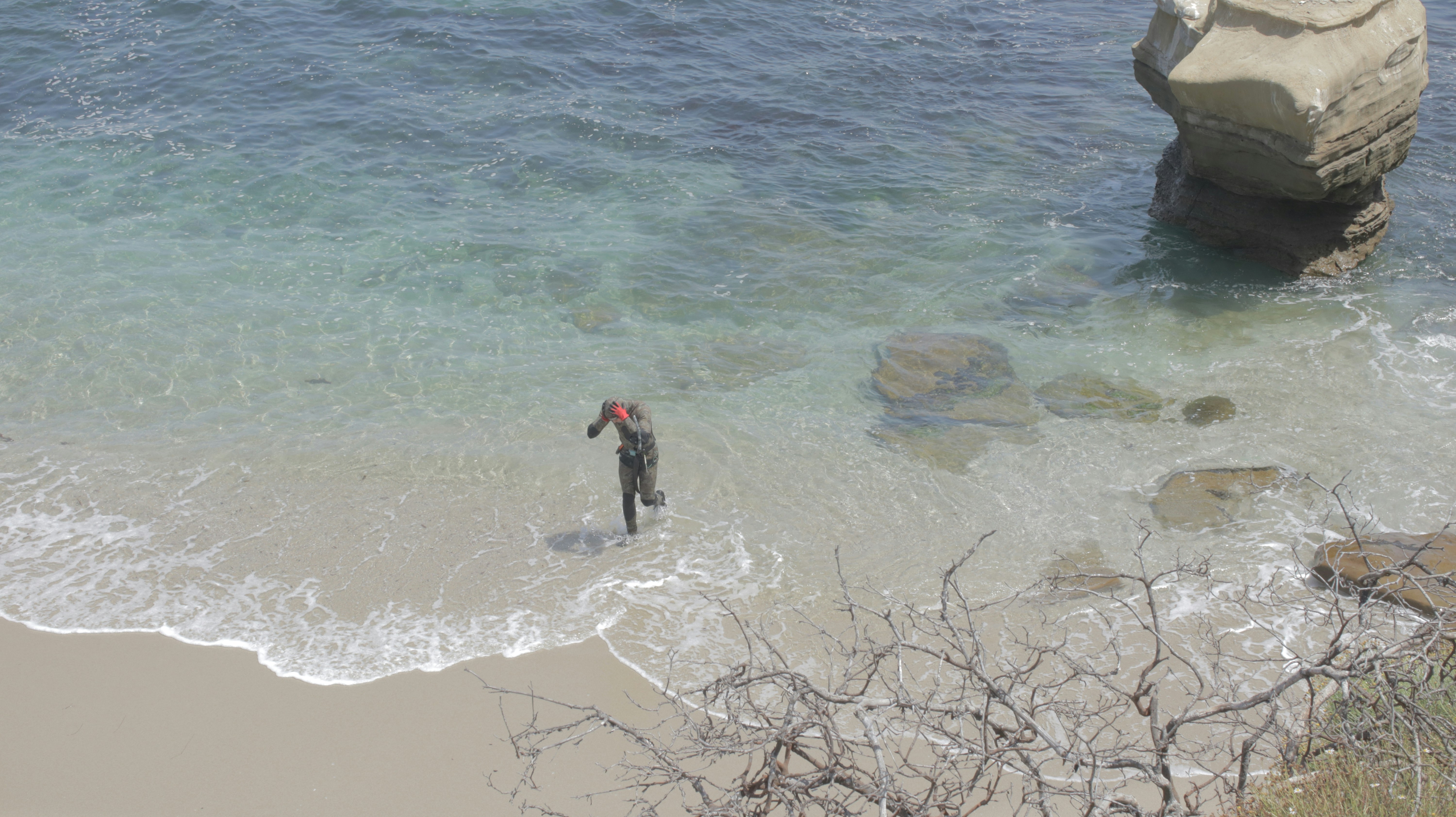 A man standing in the ocean next to a large rock