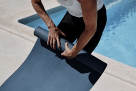 A man holding a yoga mat near a swimming pool