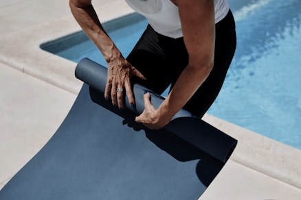 A man holding a yoga mat near a swimming pool
