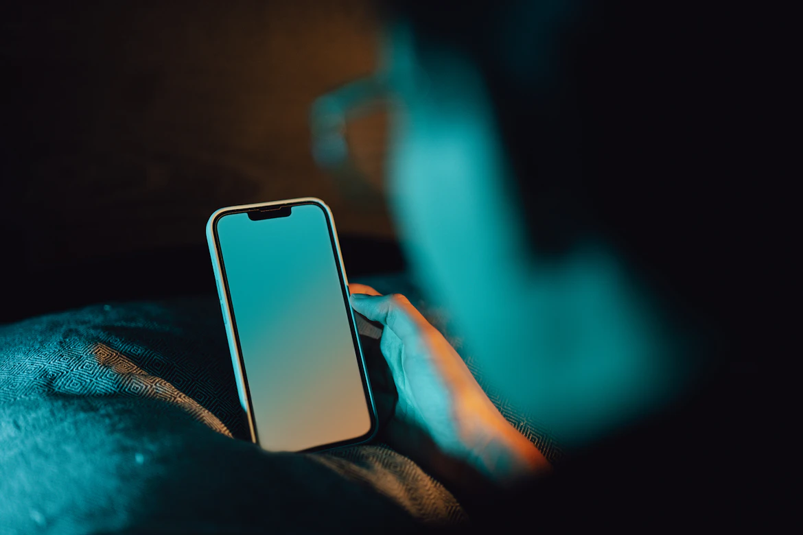 A person's hand holding a smartphone with a soft screen glow, symbolizing how AI works quietly in the background