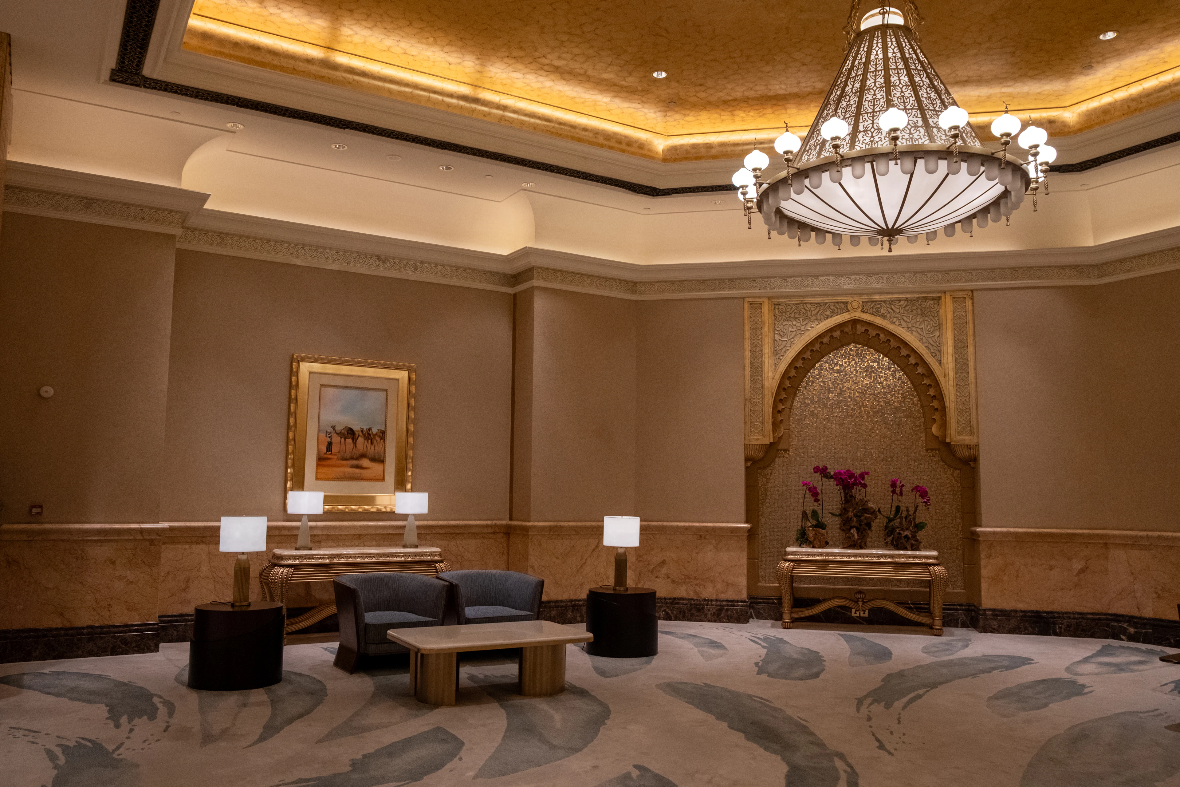 A gilded lounge inside Emirates Palace in Abu Dhabi, a great chandelier hanging beneath a gold-leaf ceiling above low sofas and a mother-of-pearl arched alcove.