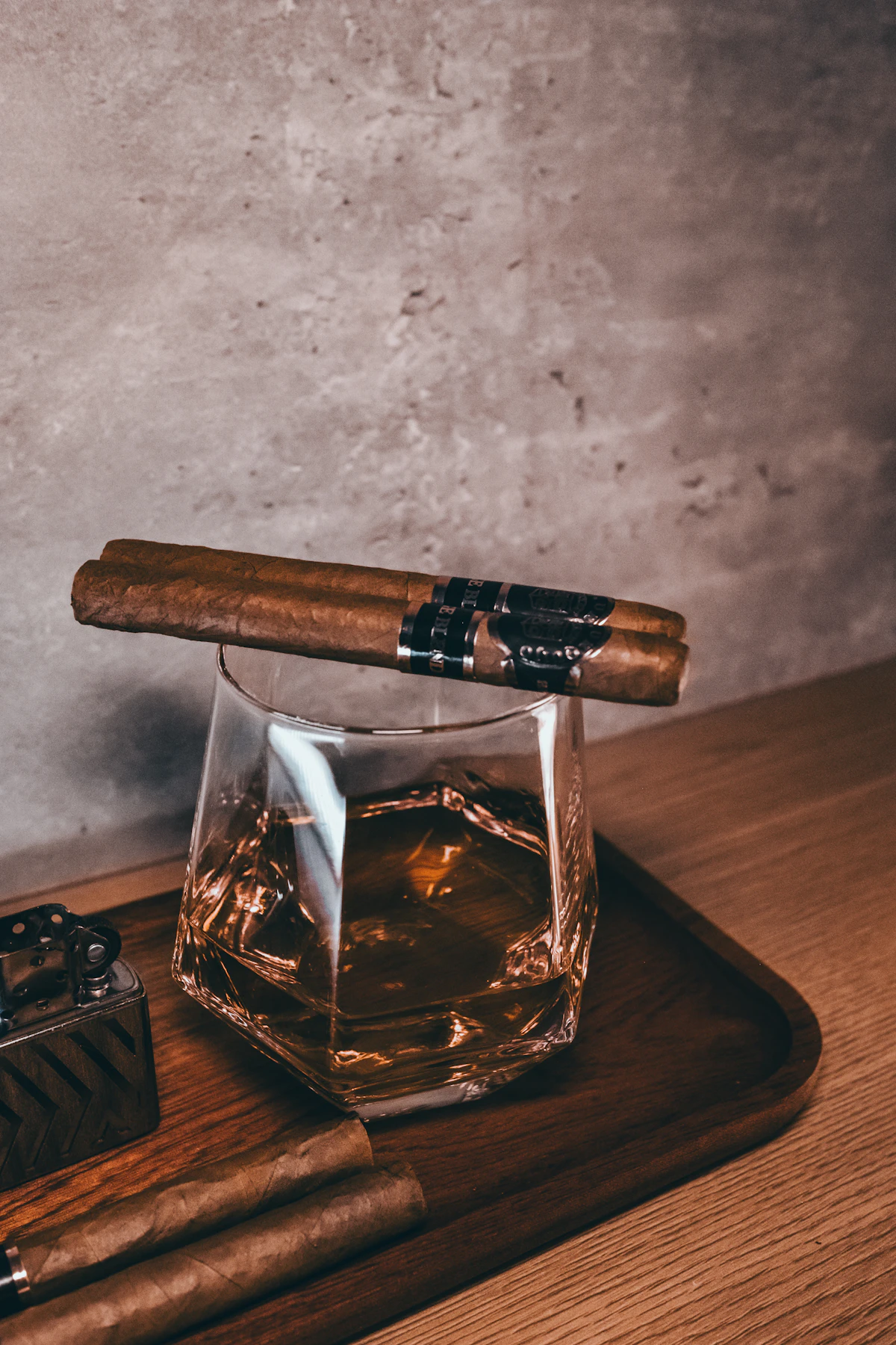 Glass of amber spirit beside a hand-rolled cigar on dark surface