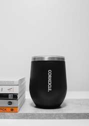 A black cup sitting on top of a table next to a stack of books