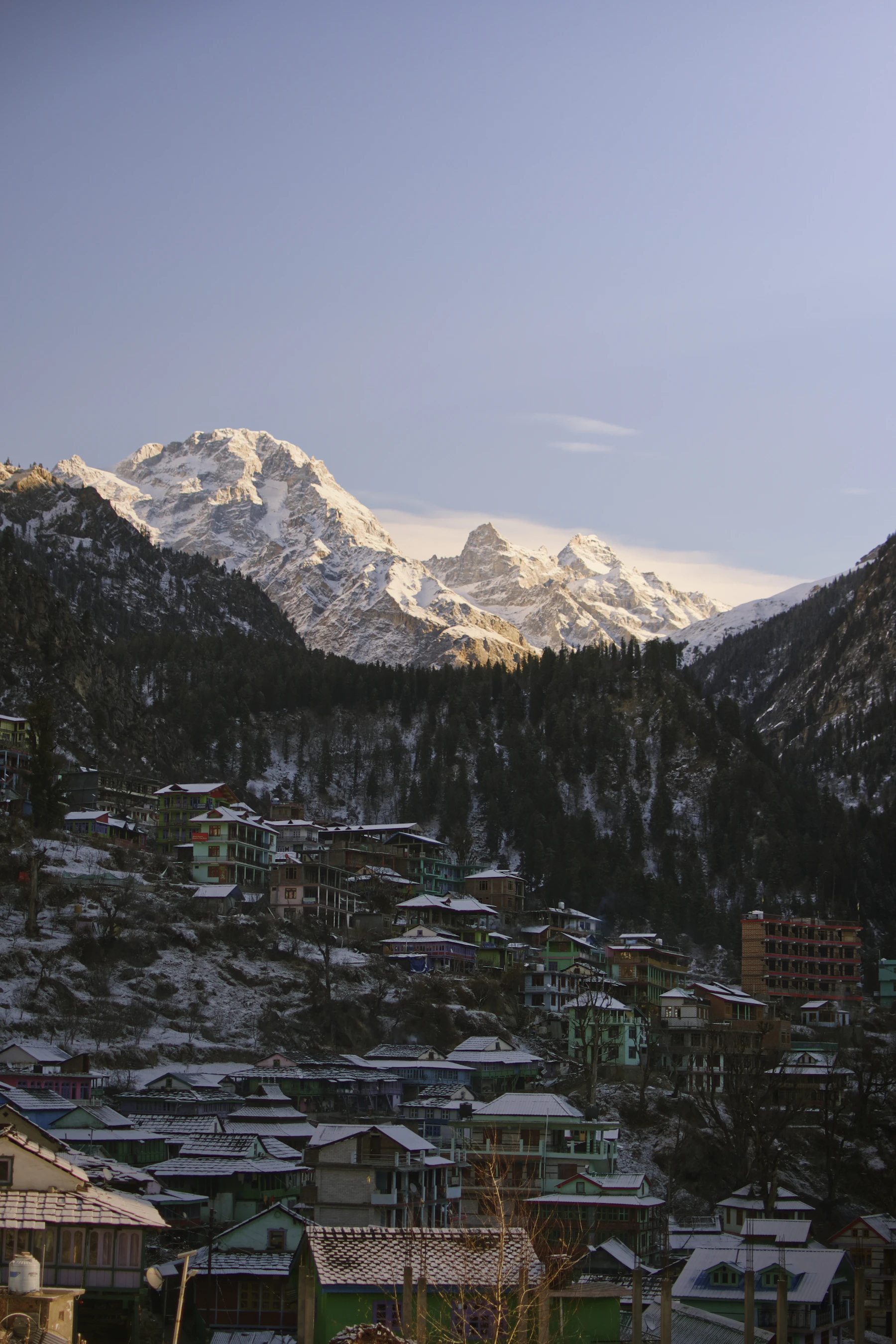Snow-dusted Himalayan mountain range with a cluster of houses on the slope below