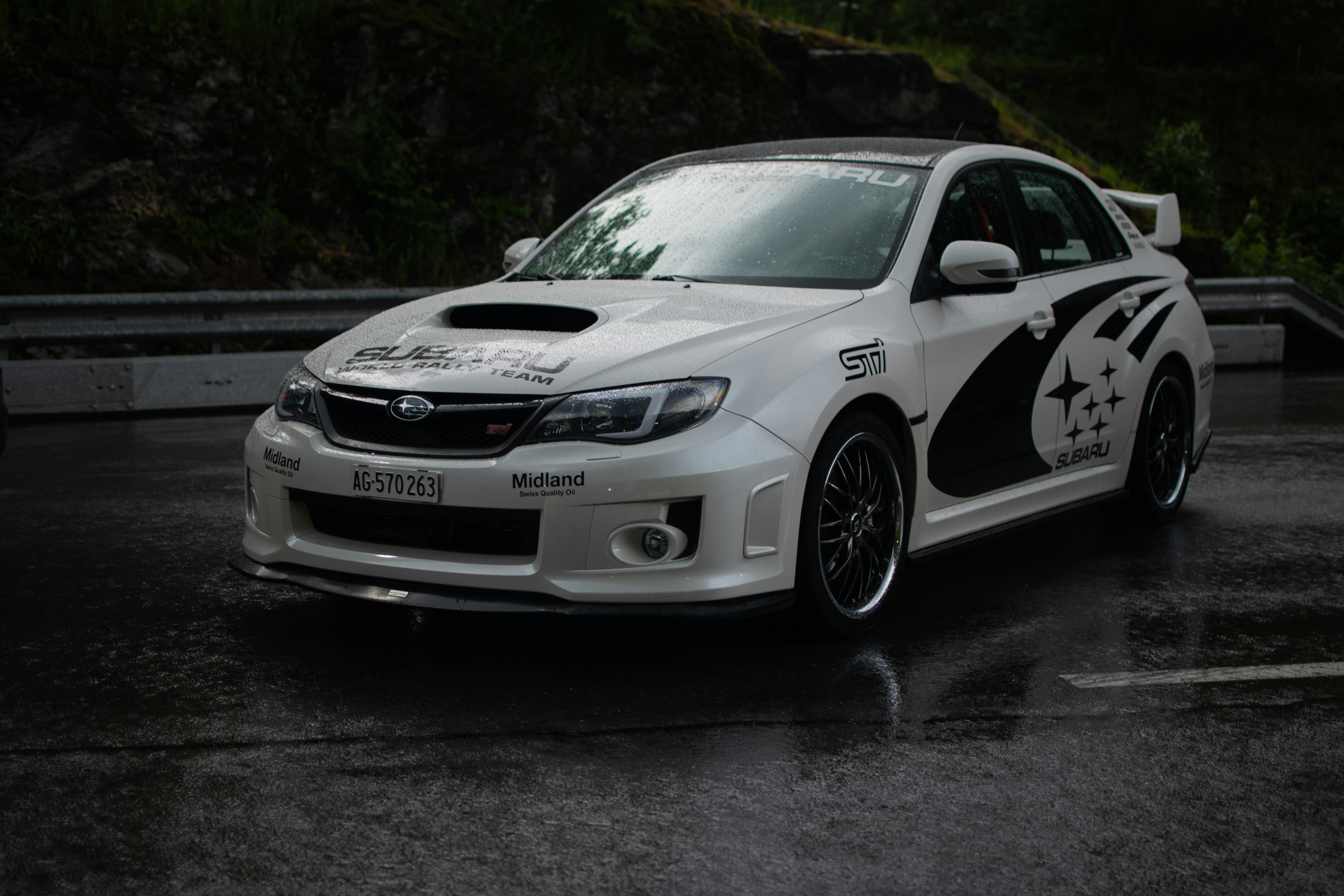 A white car parked in a parking lot on a rainy day