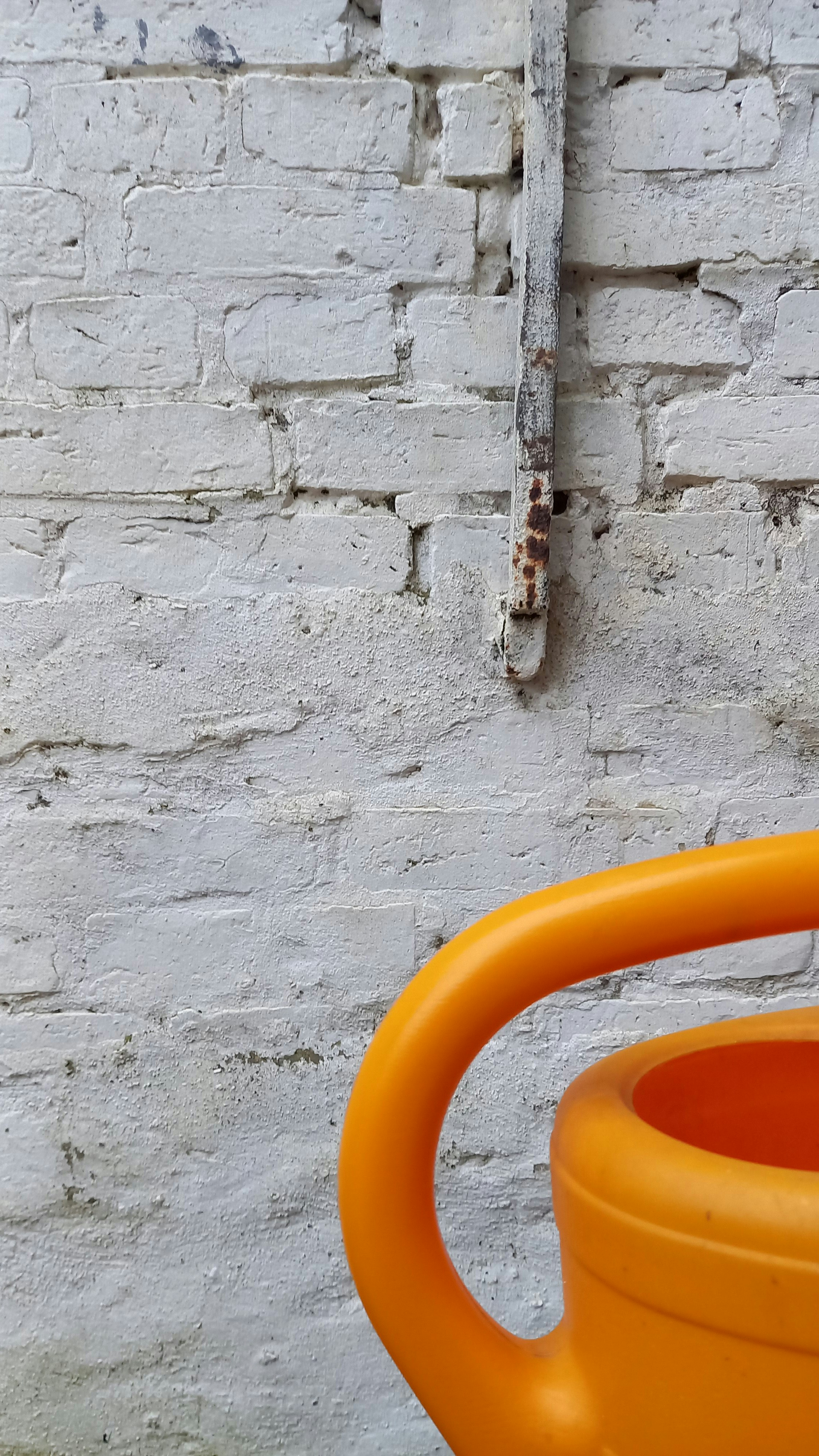 An orange watering can sitting in front of a brick wall