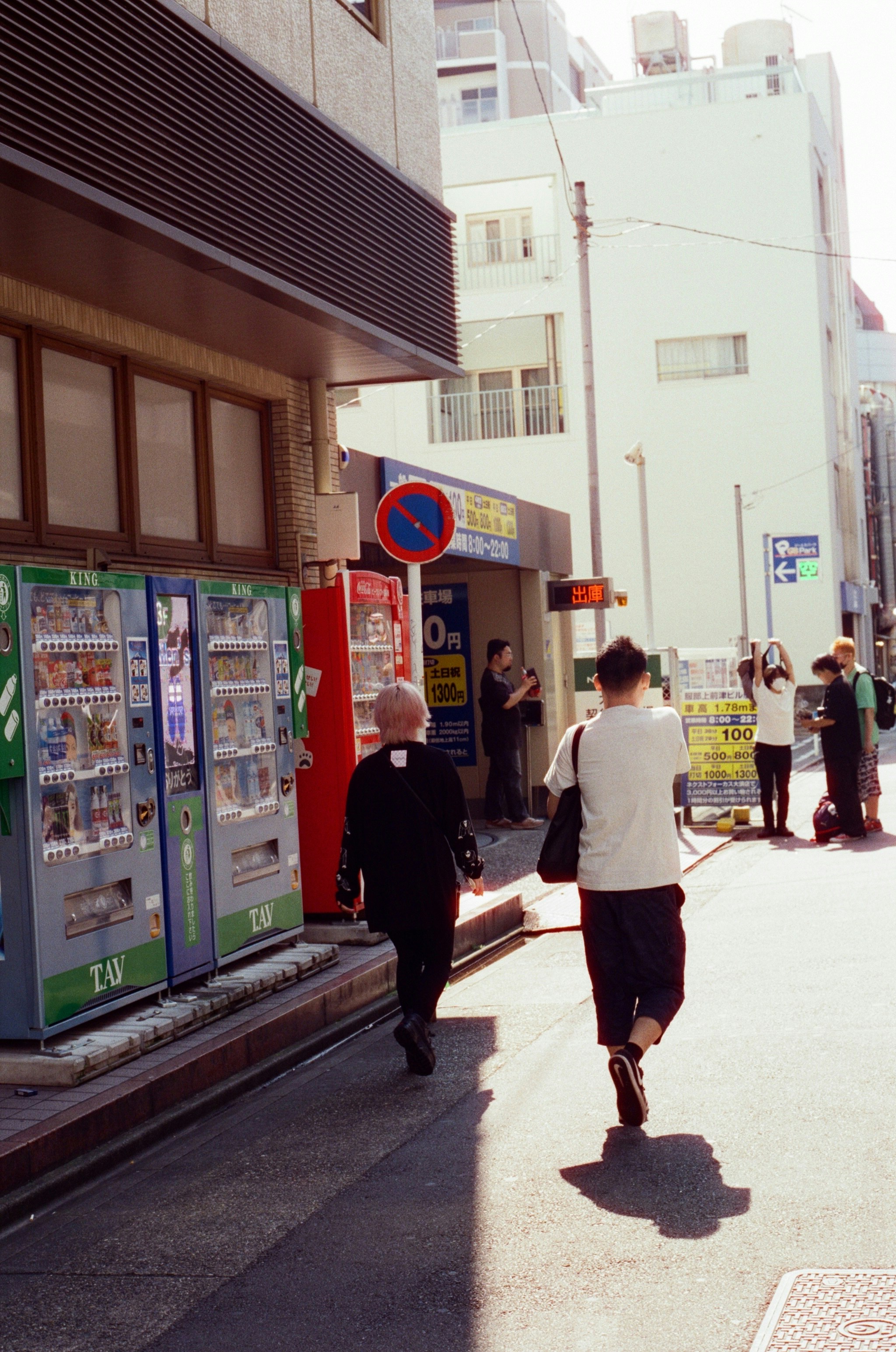 A group of people walking down a street next to vending machines