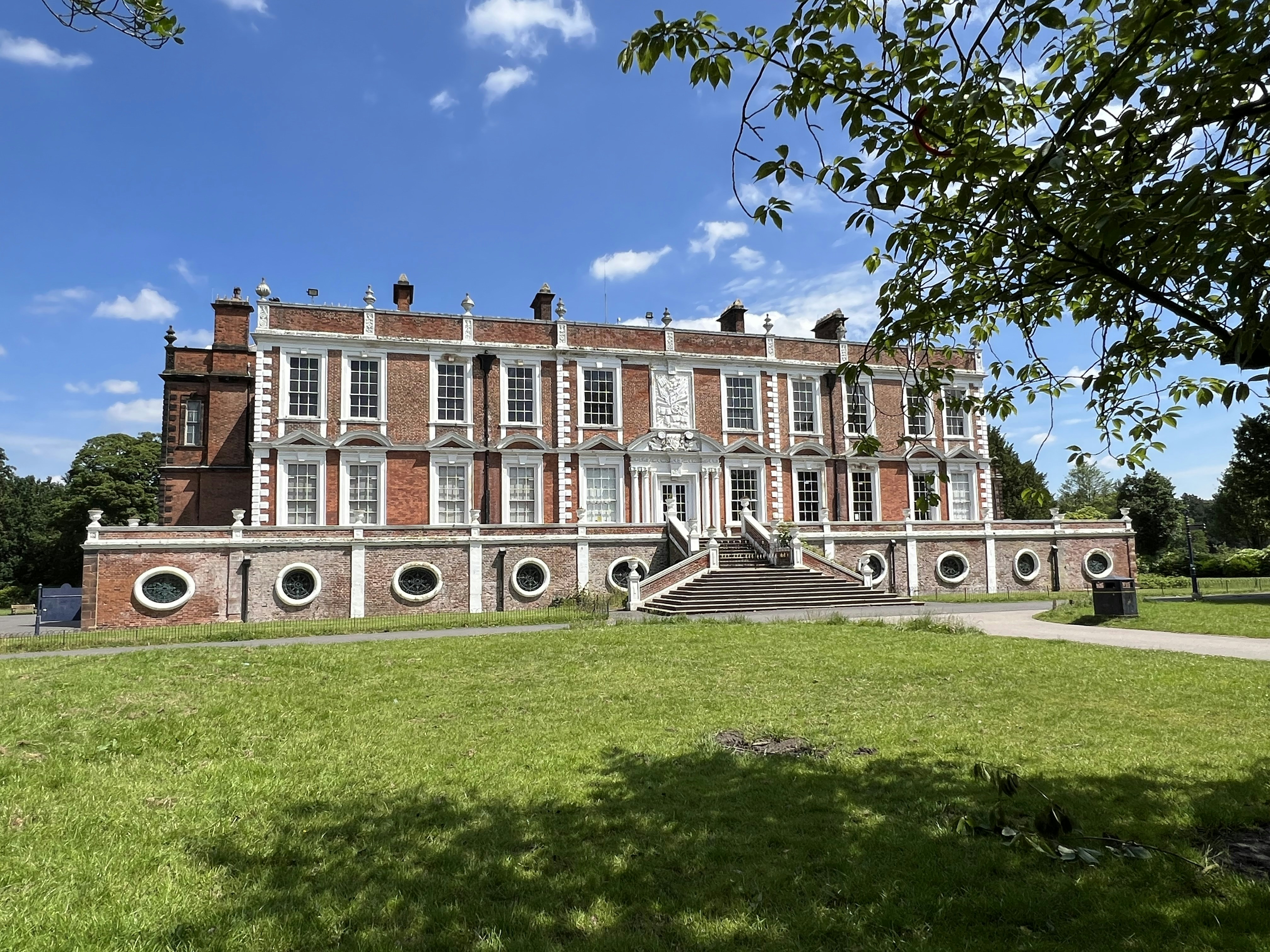 Grand colonial mansion with manicured lawns, ornate archways, and art exhibits visible through tall arched windows