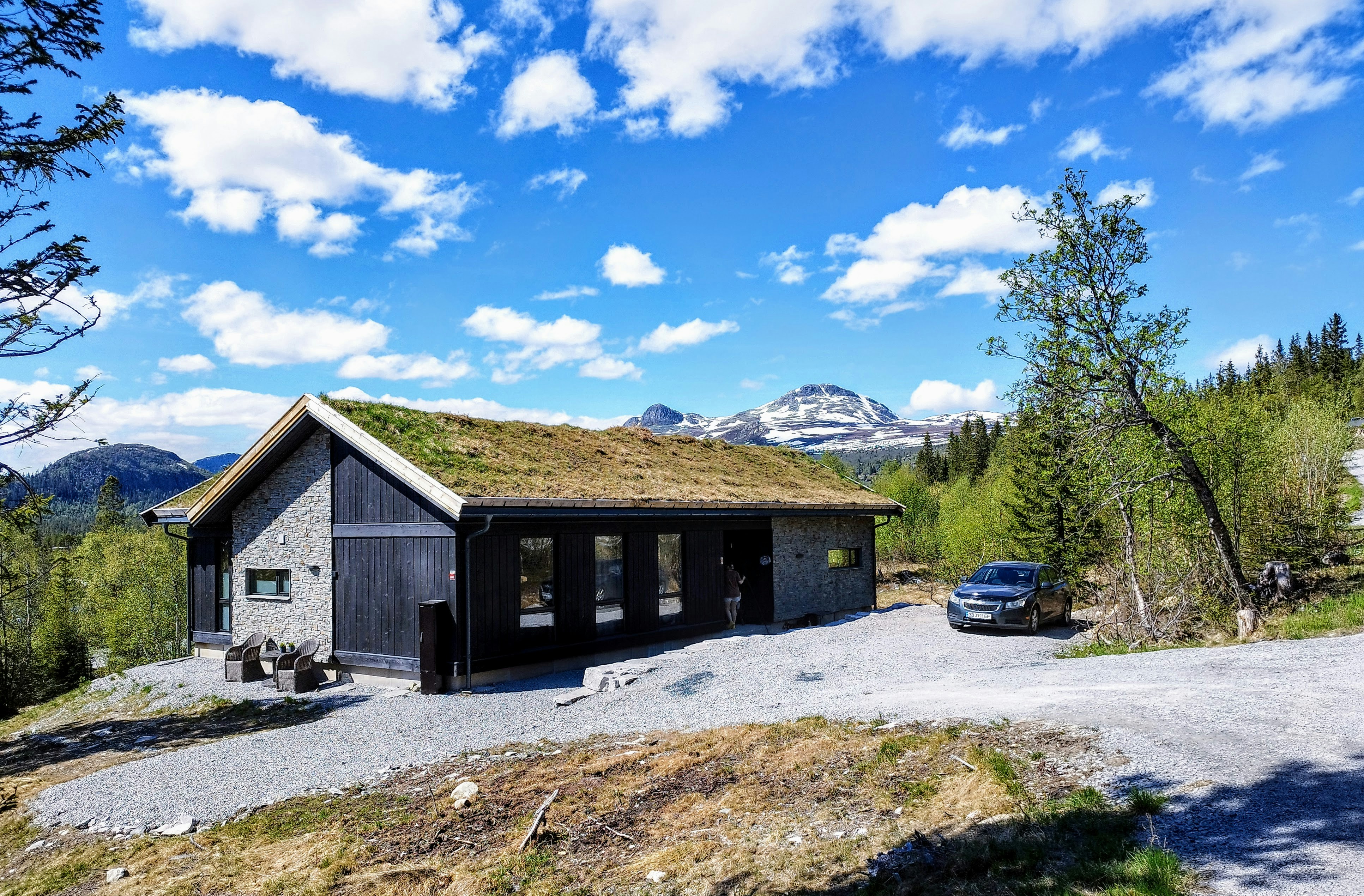 Mørk hytte med torvtak og grusplass i fjellet