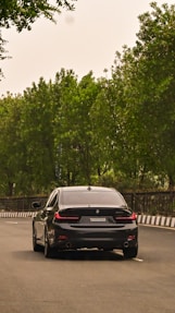 A black car driving down a street next to trees