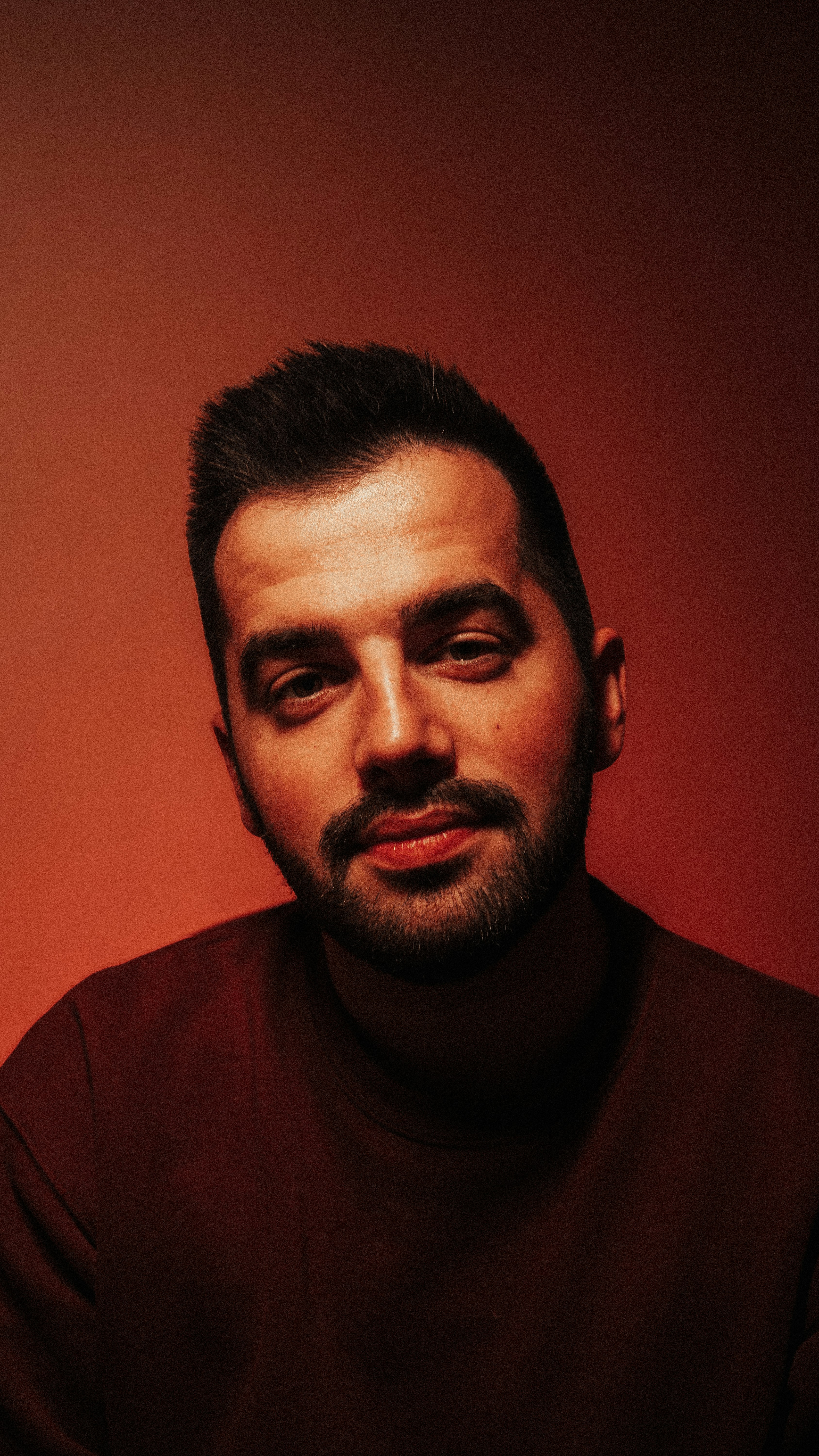 A man with a goatee and beard sitting in front of a red wall
