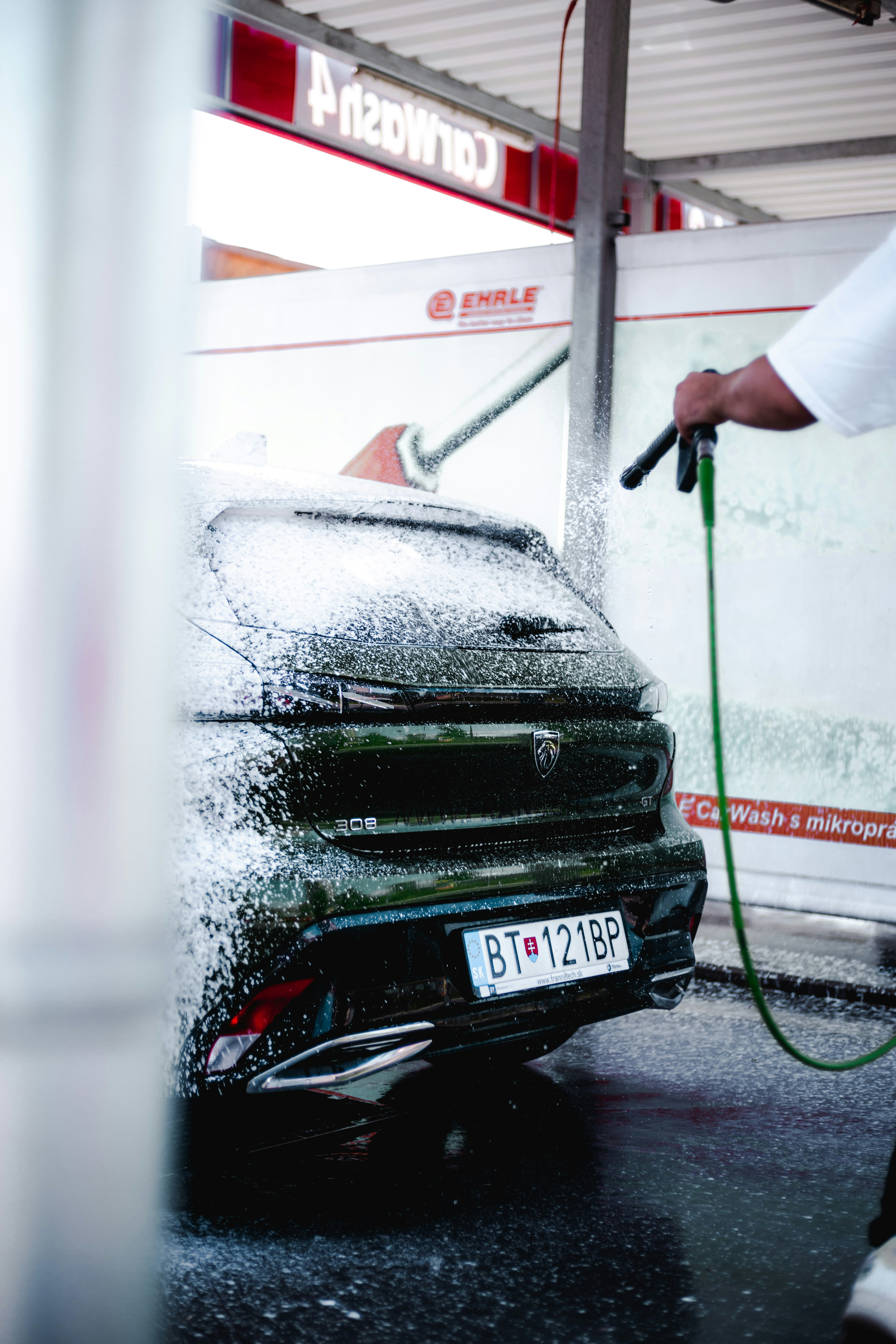 Professional car wash service with water spray on dark vehicle exterior