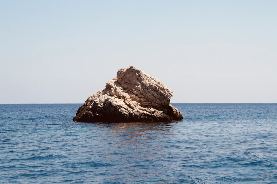 Serene rock formation at sea, composed of multiple layers of light brown stone
